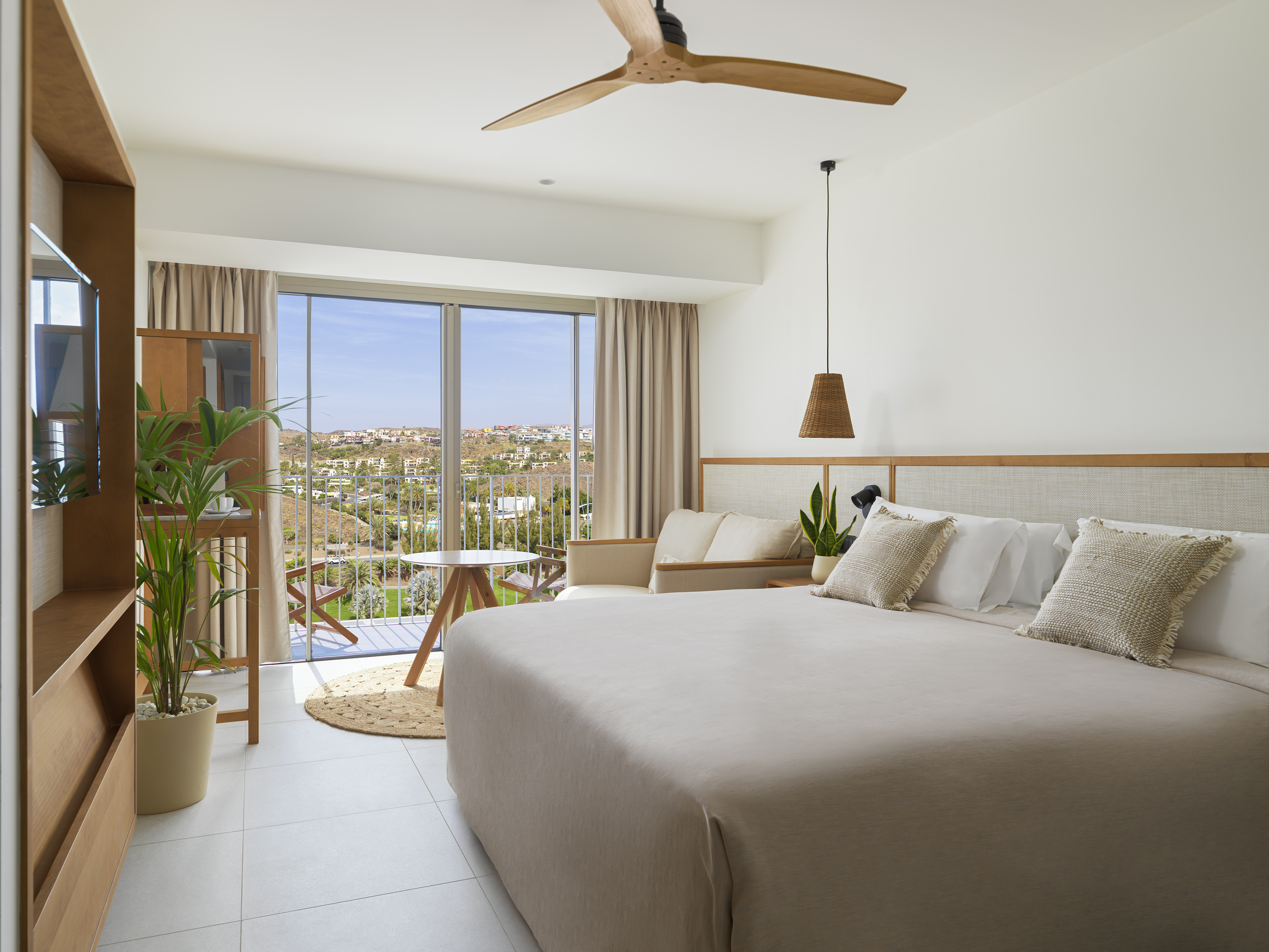 Modern hotel bedroom with balcony, large bed, and bright resort landscape view.