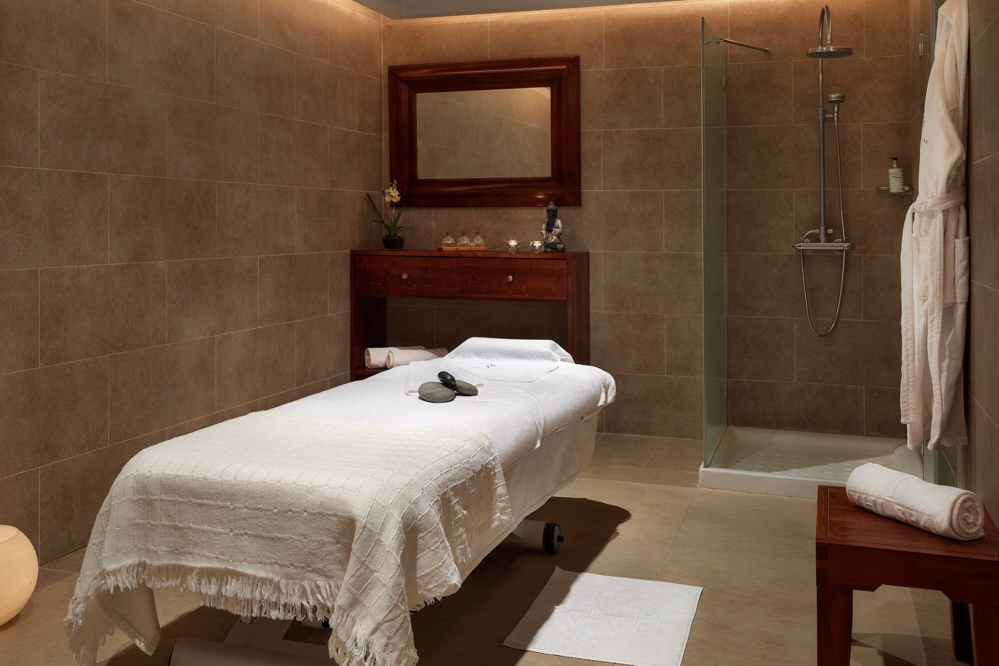 Luxury spa treatment room with massage bed, shower, and warm lighting.