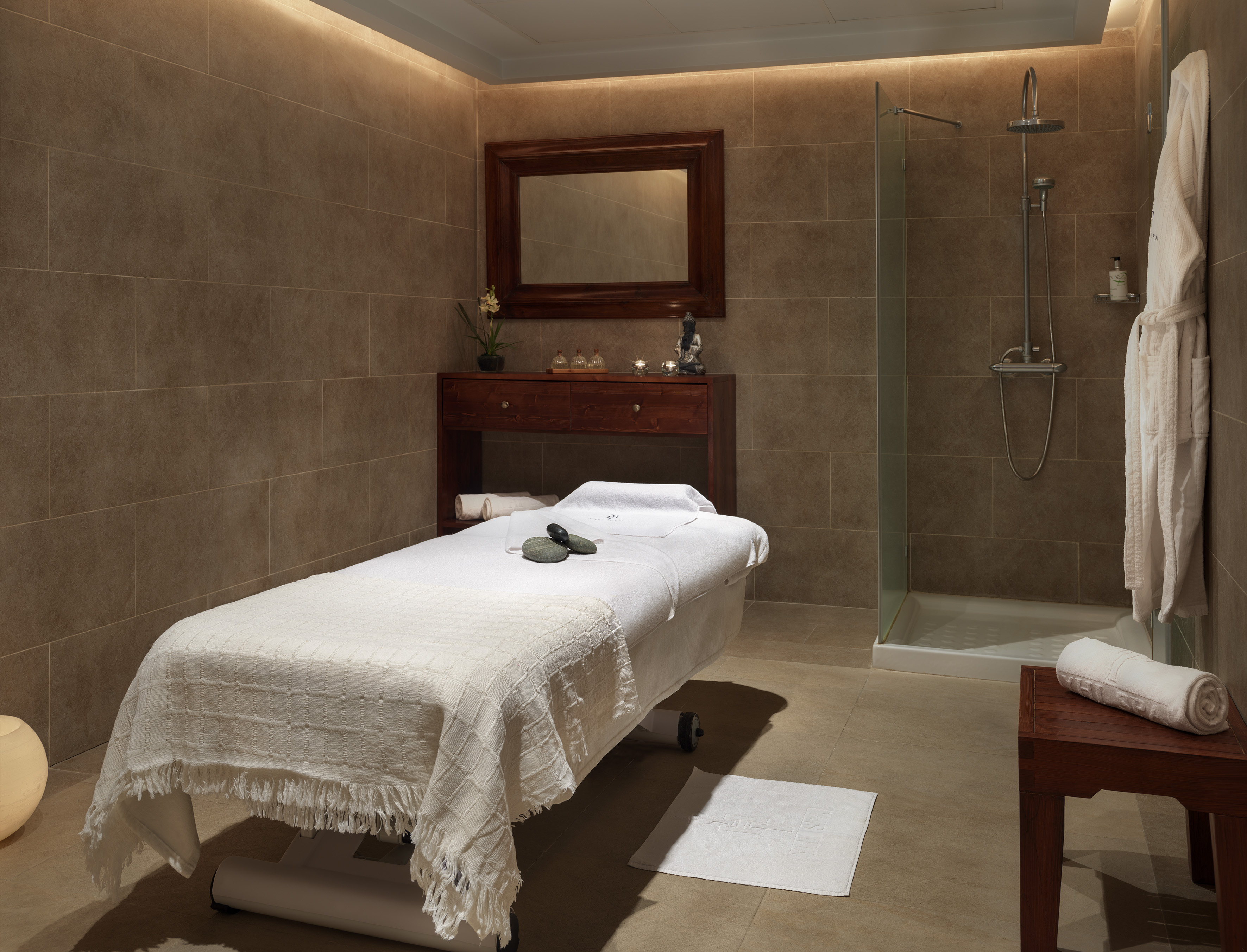 Luxury spa treatment room with massage bed, shower, and warm lighting.