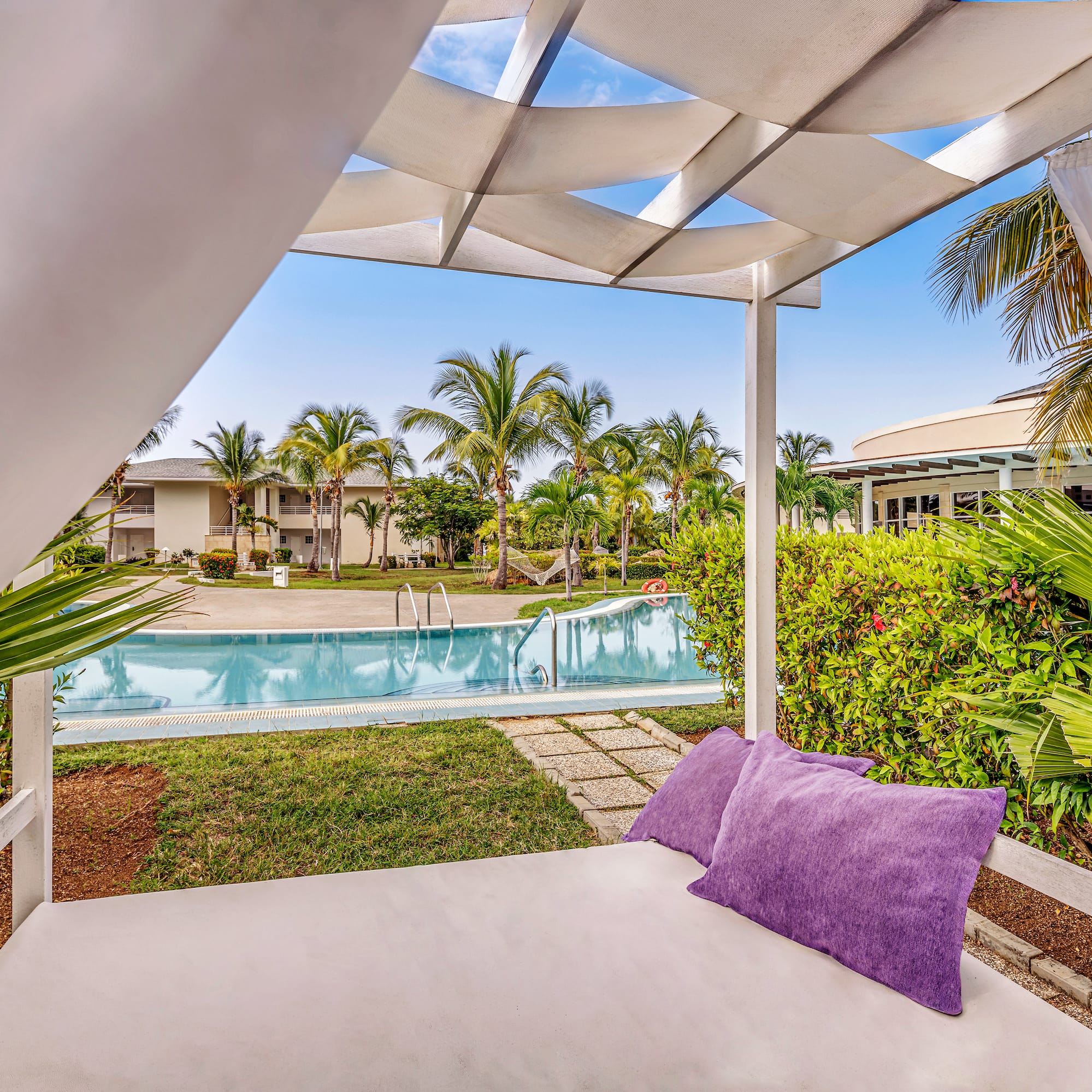 a white canopy with purple pillows and a pool in the background