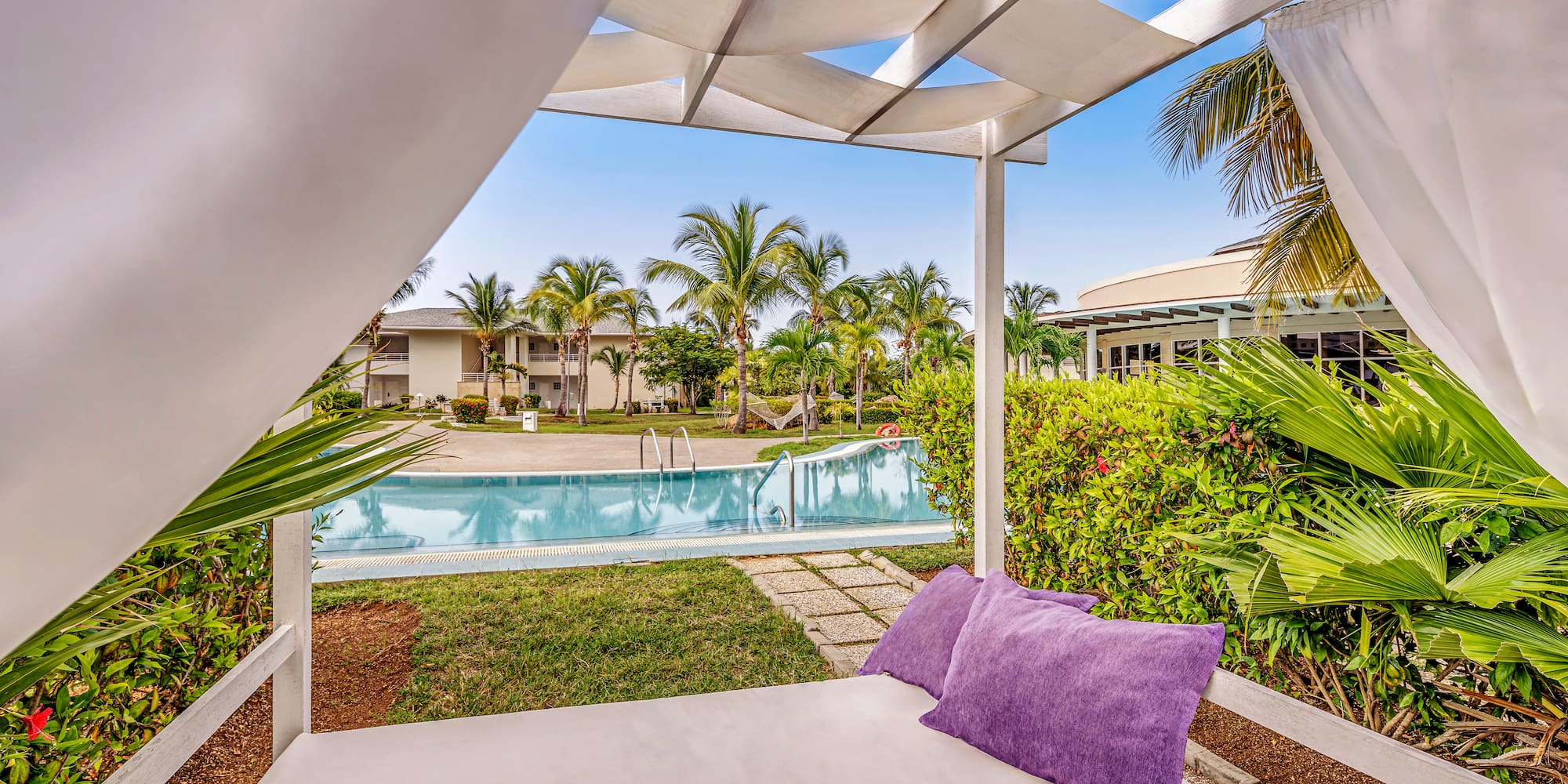 a white canopy with purple pillows and a pool in the background