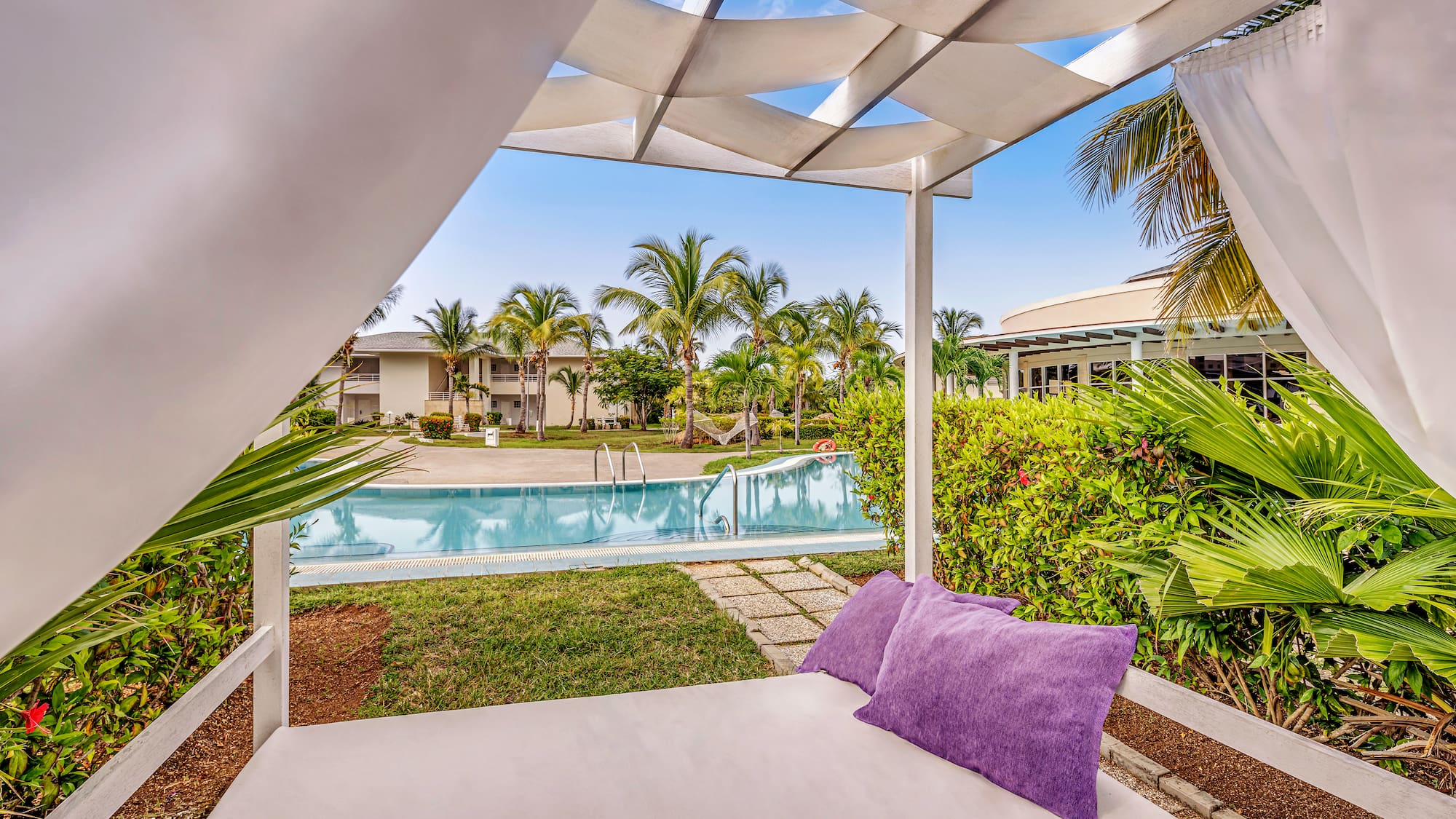 a white canopy with purple pillows and a pool in the background
