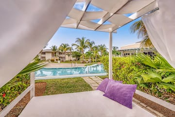 a white canopy with purple pillows and a pool in the background