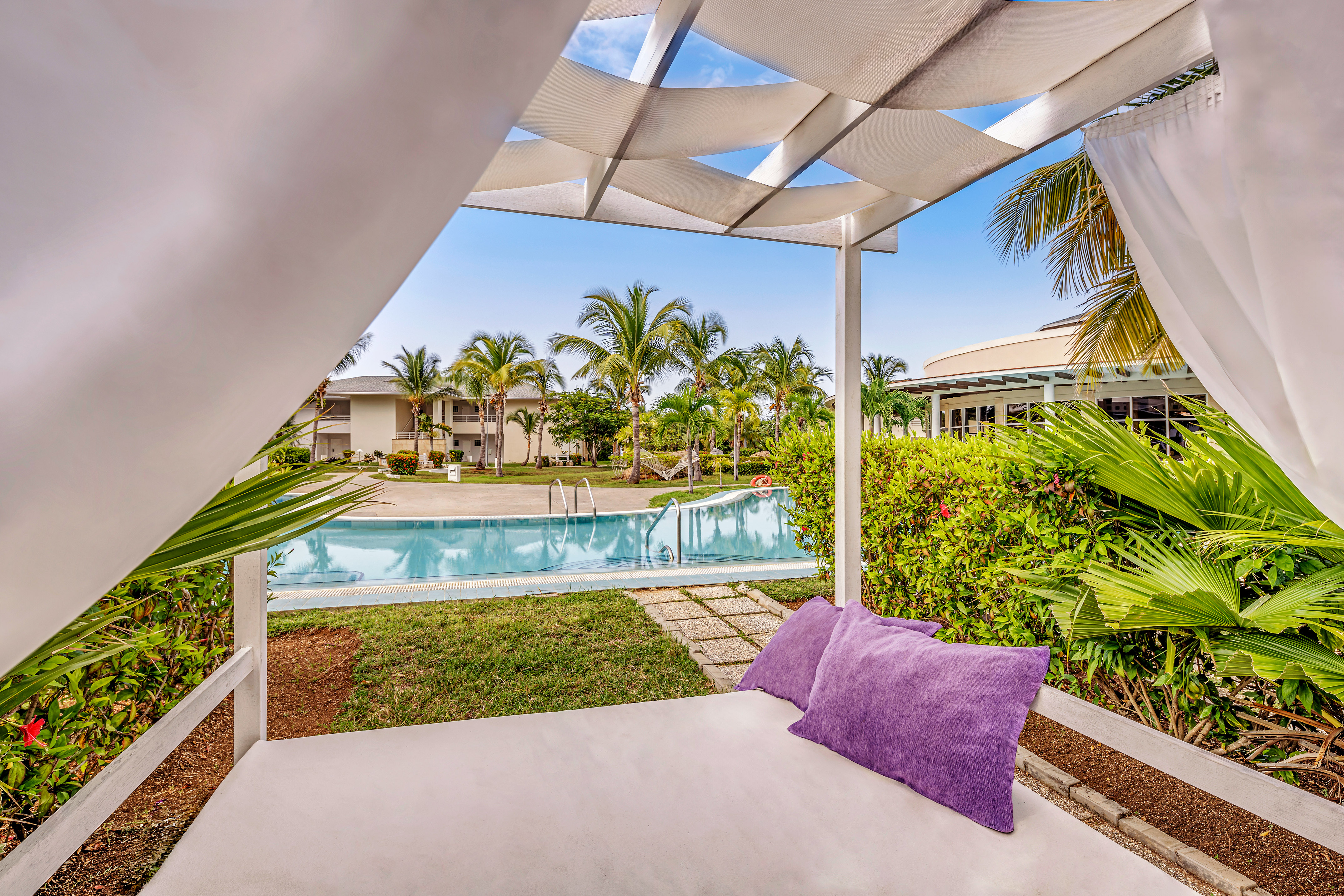 a white canopy with purple pillows and a pool in the background