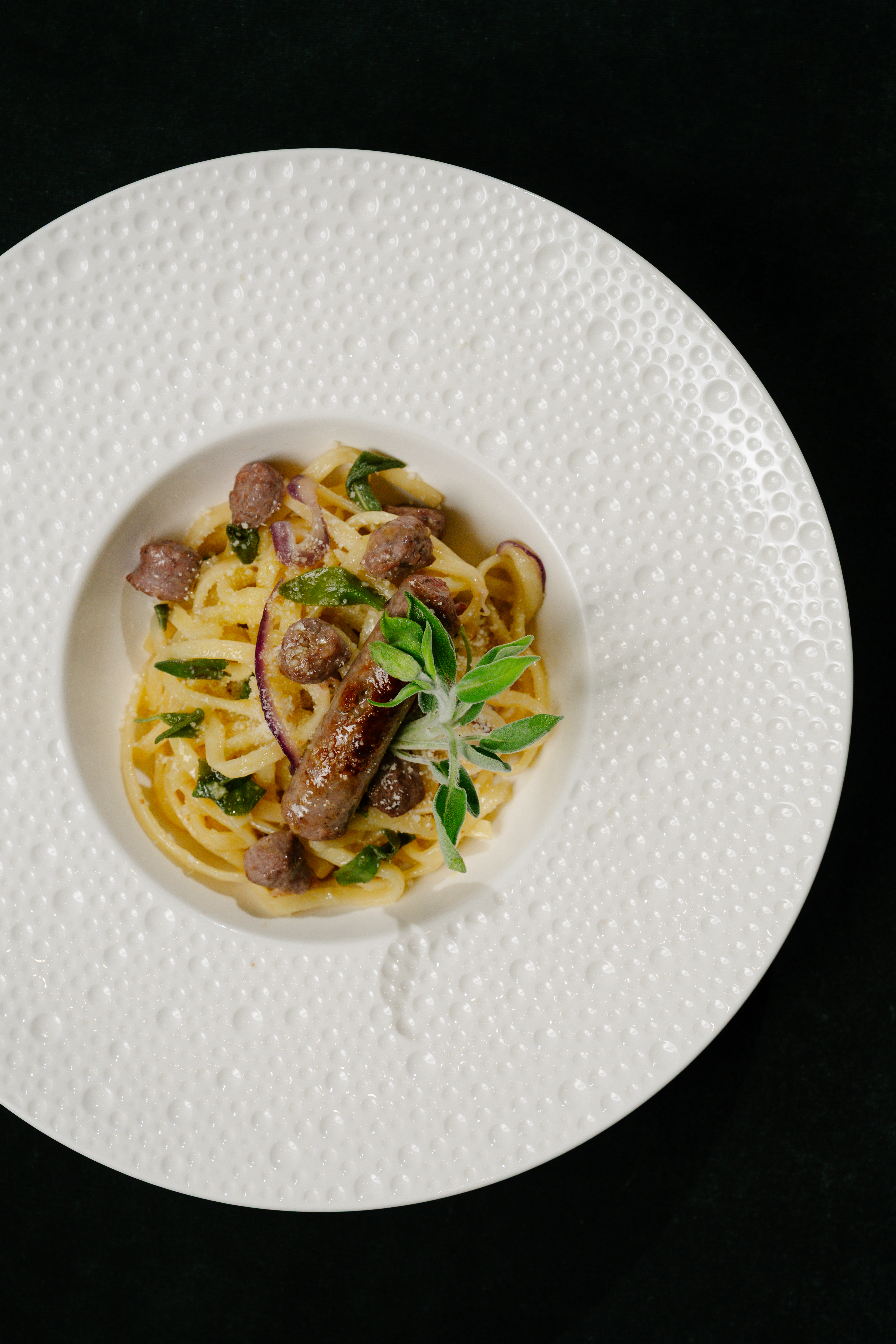Sausage pasta with red onion, sage, and creamy sauce in a textured white bowl.
