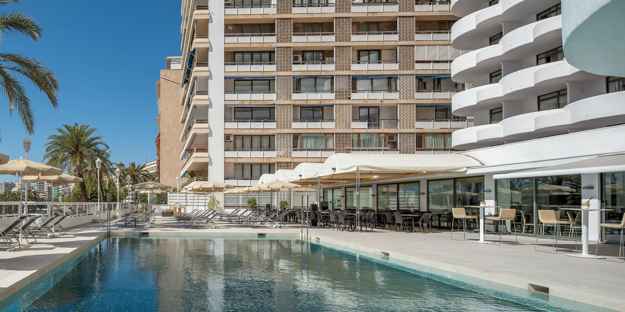 a pool with chairs and tables in front of a building