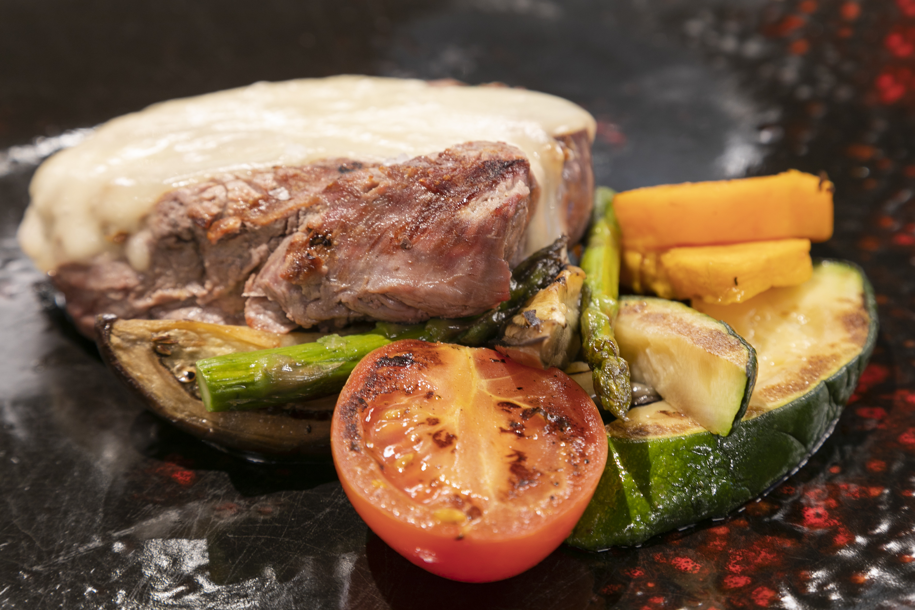 Grilled steak with melted cheese, asparagus, zucchini, tomato, and squash.