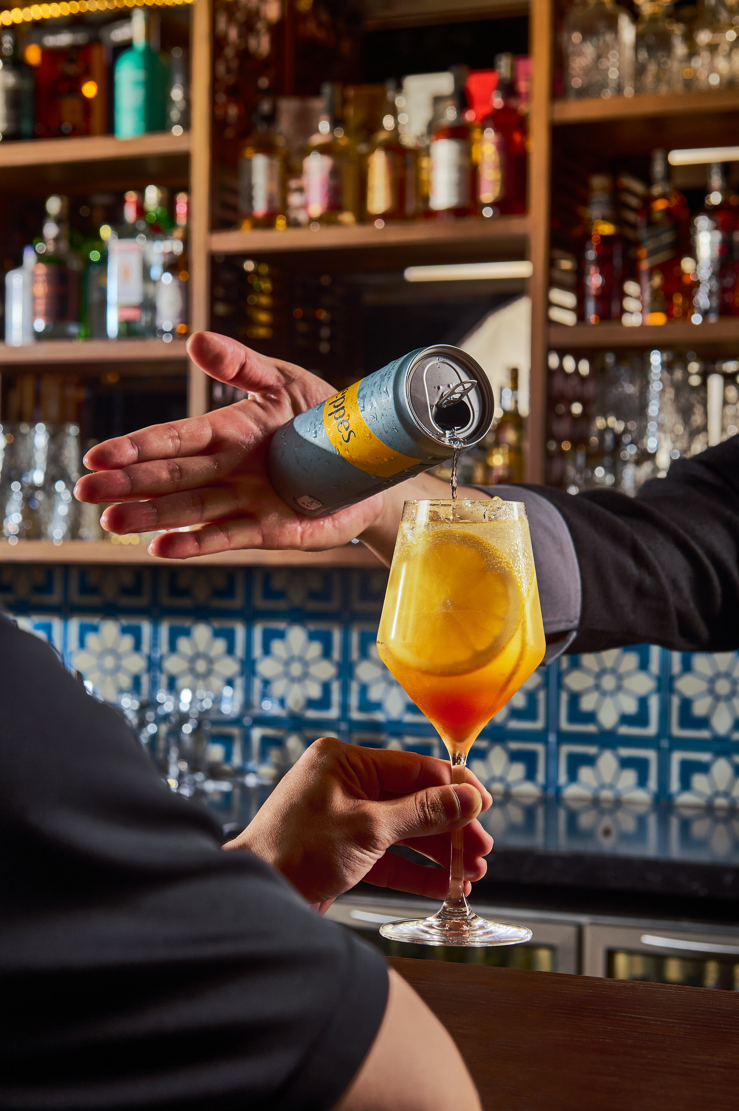 Pouring Schweppes from can into an orange cocktail glass at a bar.