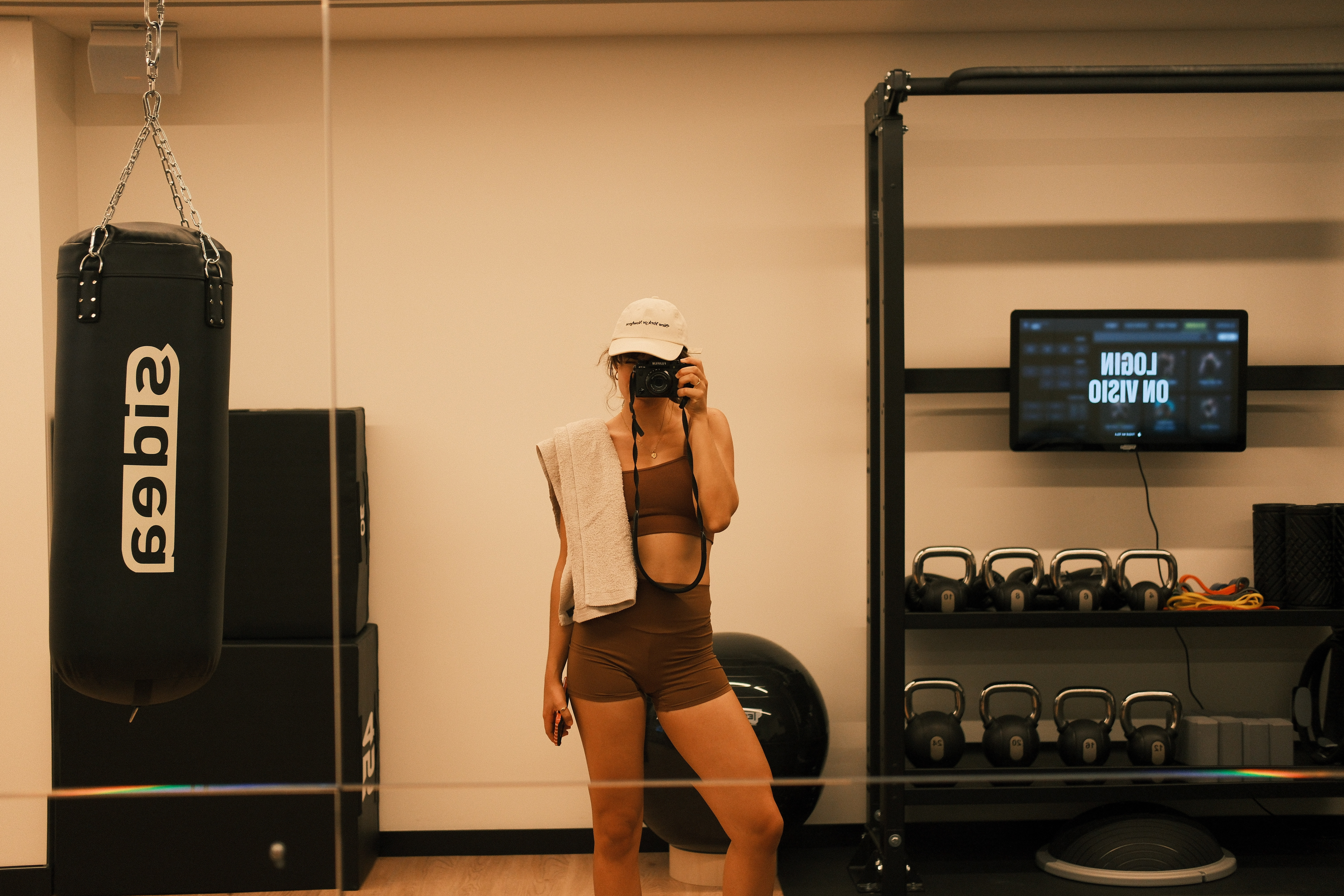 Gym selfie: Woman in brown activewear with punching bag and kettlebells.