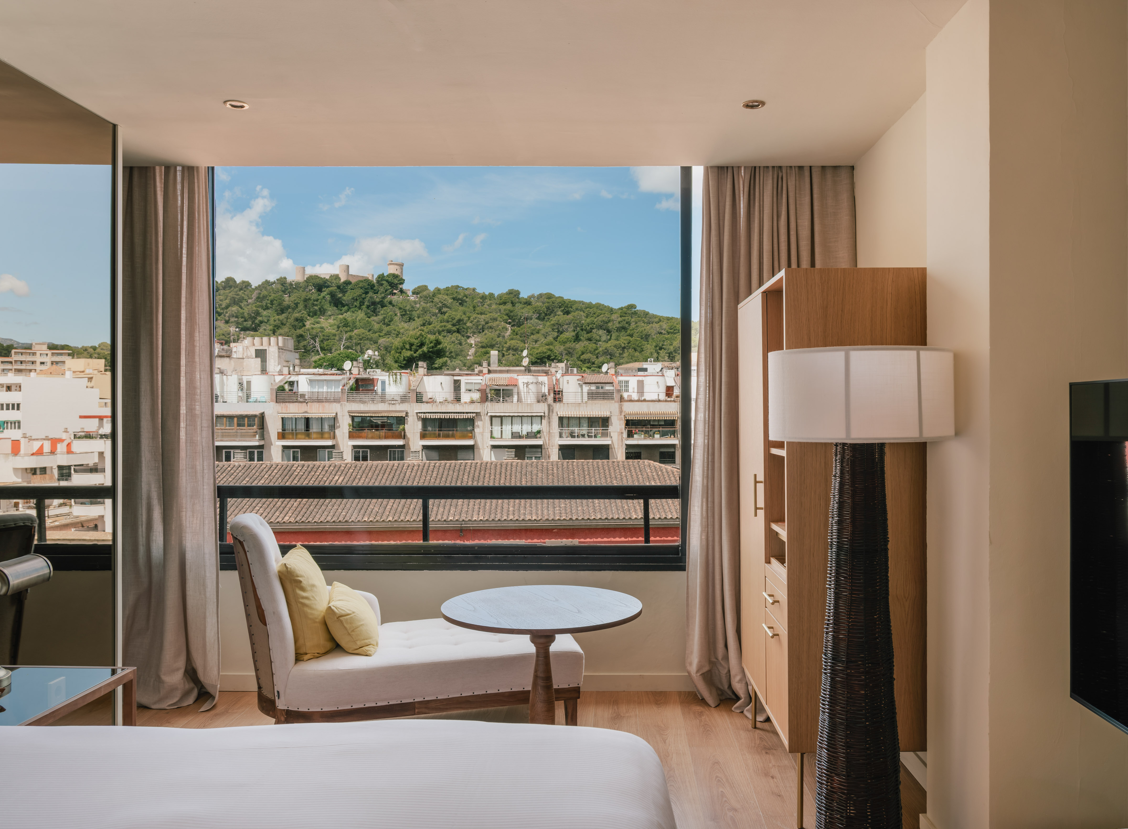 Hotel room with large window, city views, and distant Bellver Castle.