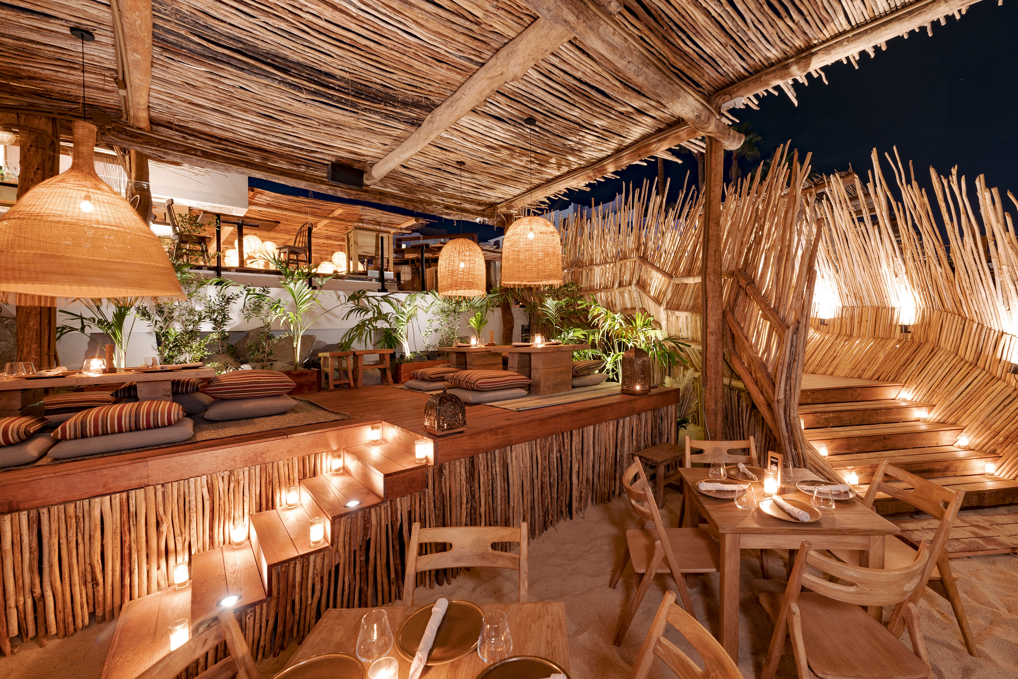 Tropical outdoor dining with warm lighting, natural wood, bamboo, and cozy seating.