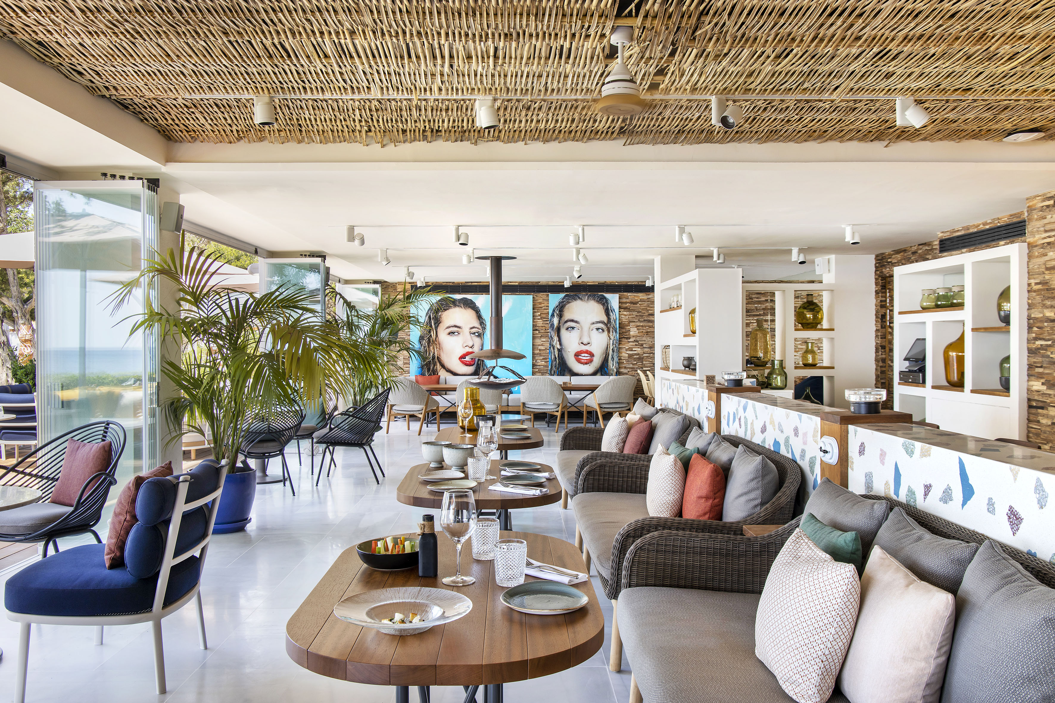 Chic beachfront restaurant interior with bamboo ceiling, modern art, and set tables.