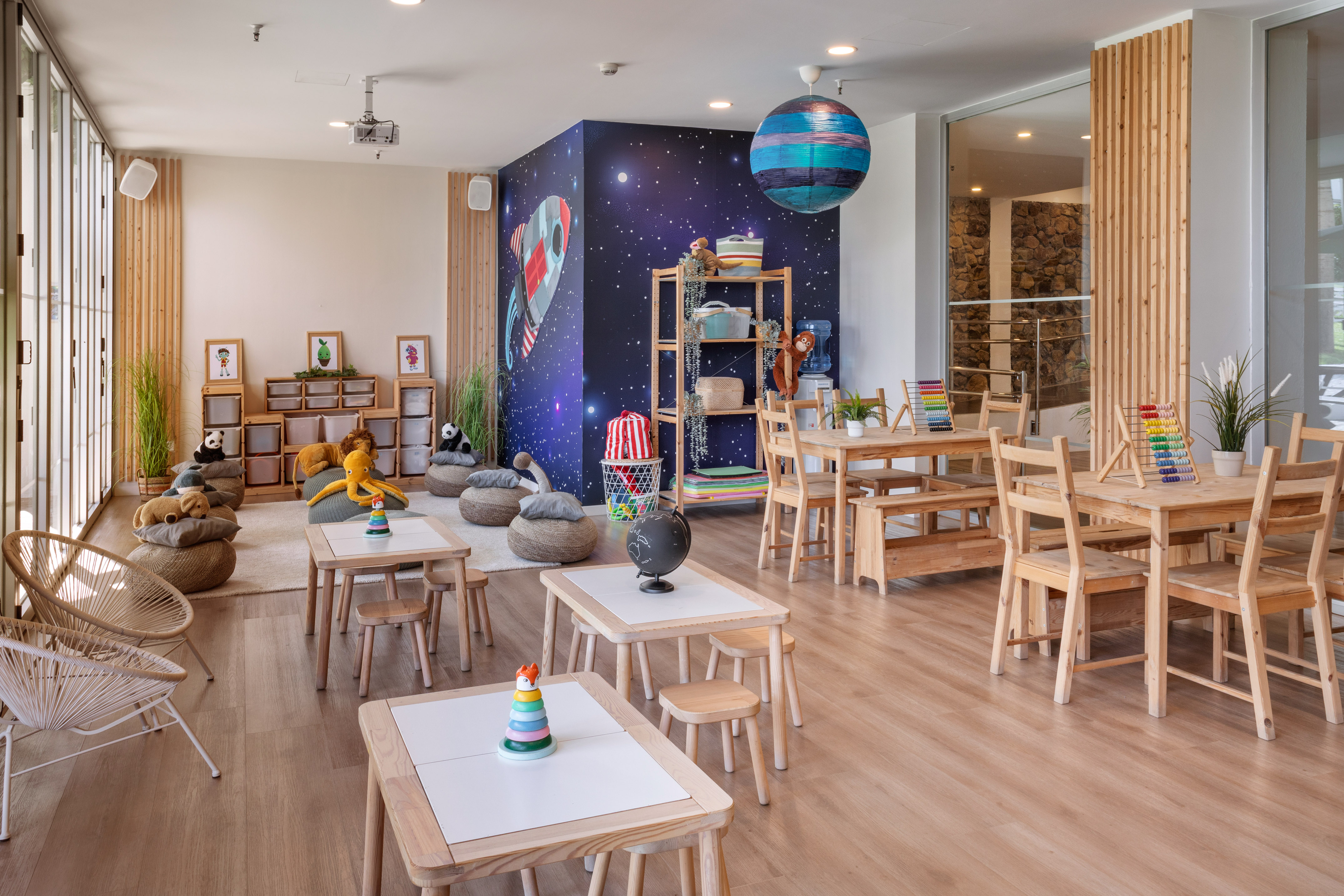 Kids club playroom with space mural, wooden tables, beanbags, and learning toys.