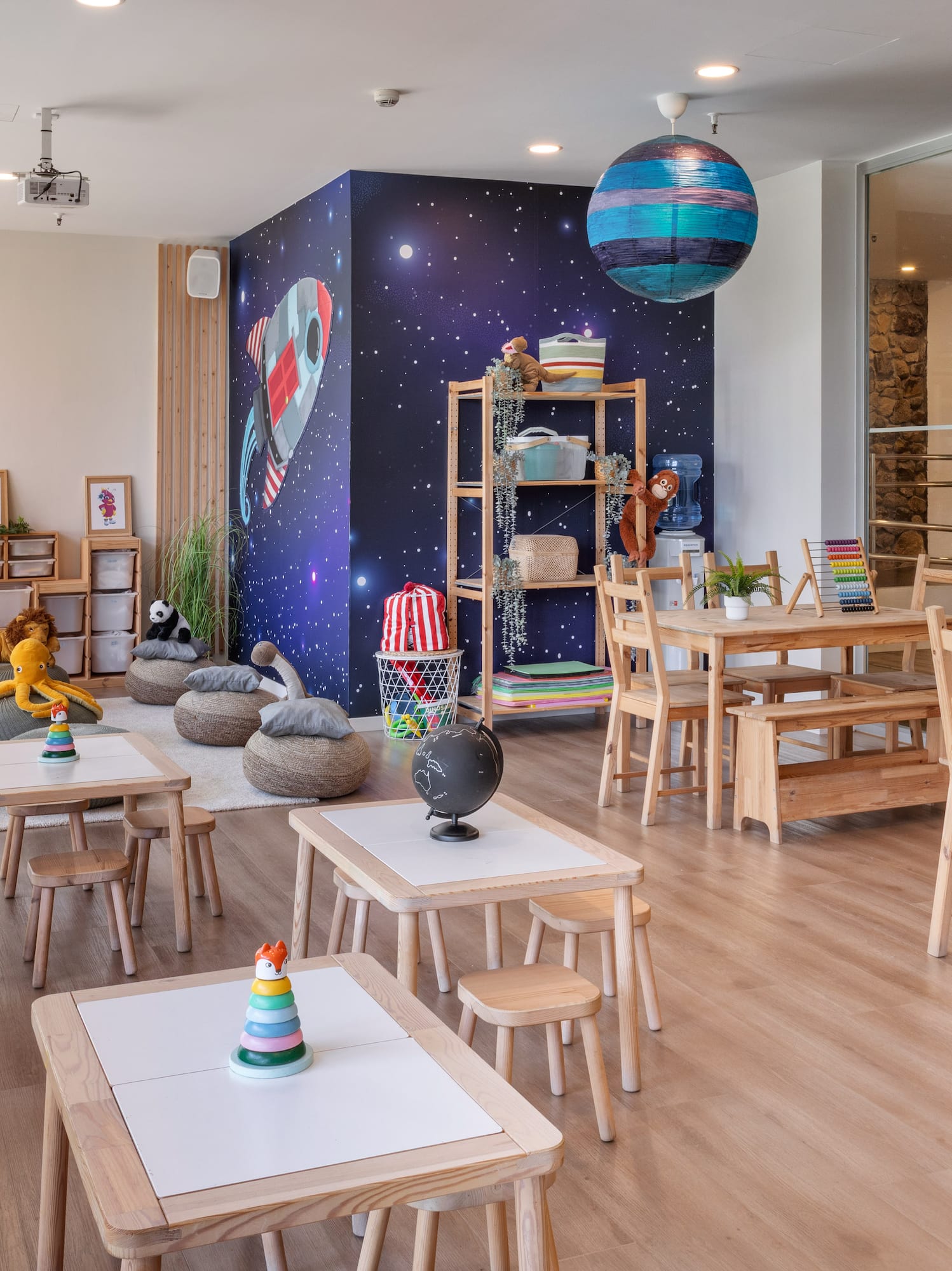 Kids club playroom with space mural, wooden tables, beanbags, and learning toys.