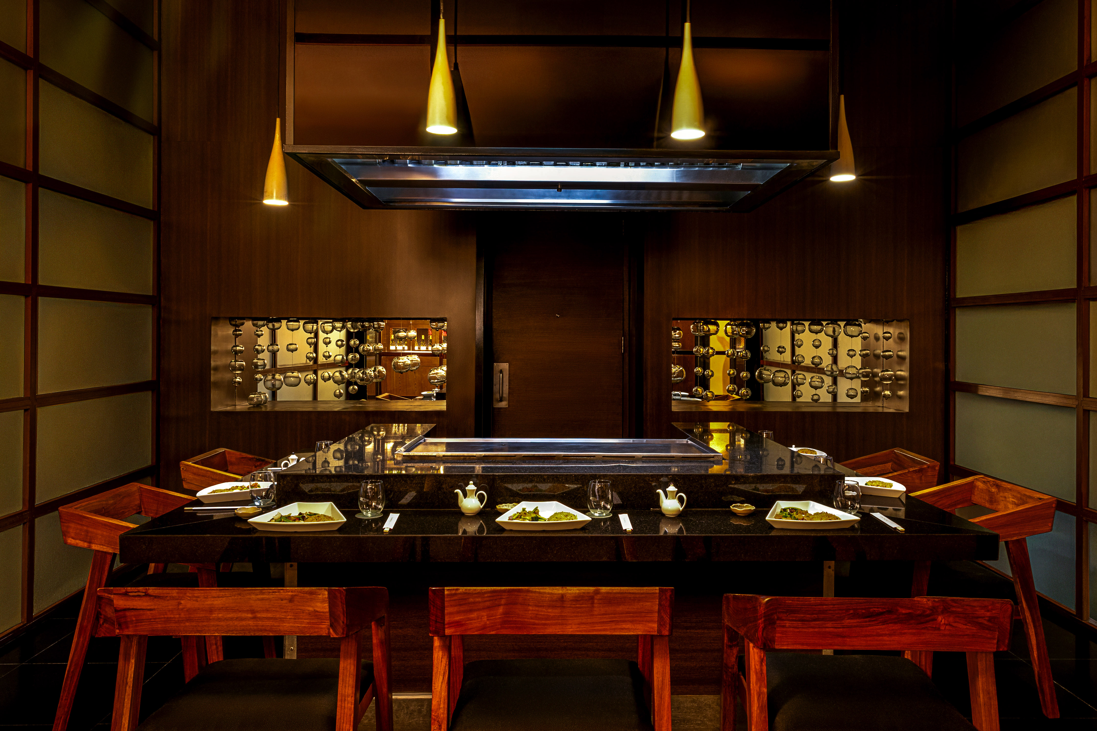 Dark wood teppanyaki restaurant with central grill and modern gold pendant lights.