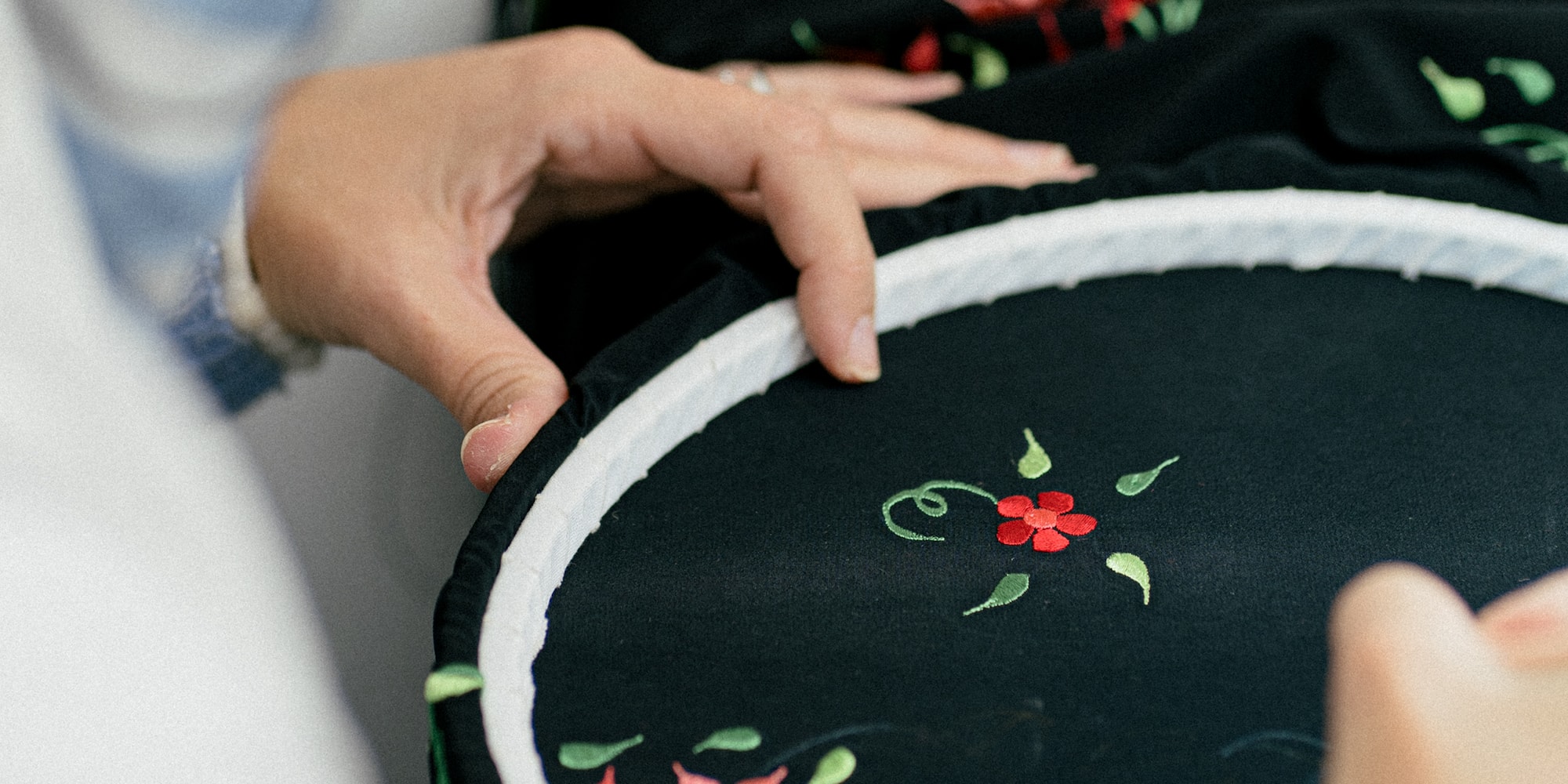 a person sewing a black fabric with a red flower on it