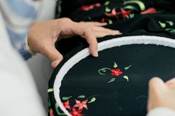 a person sewing a black fabric with a red flower on it