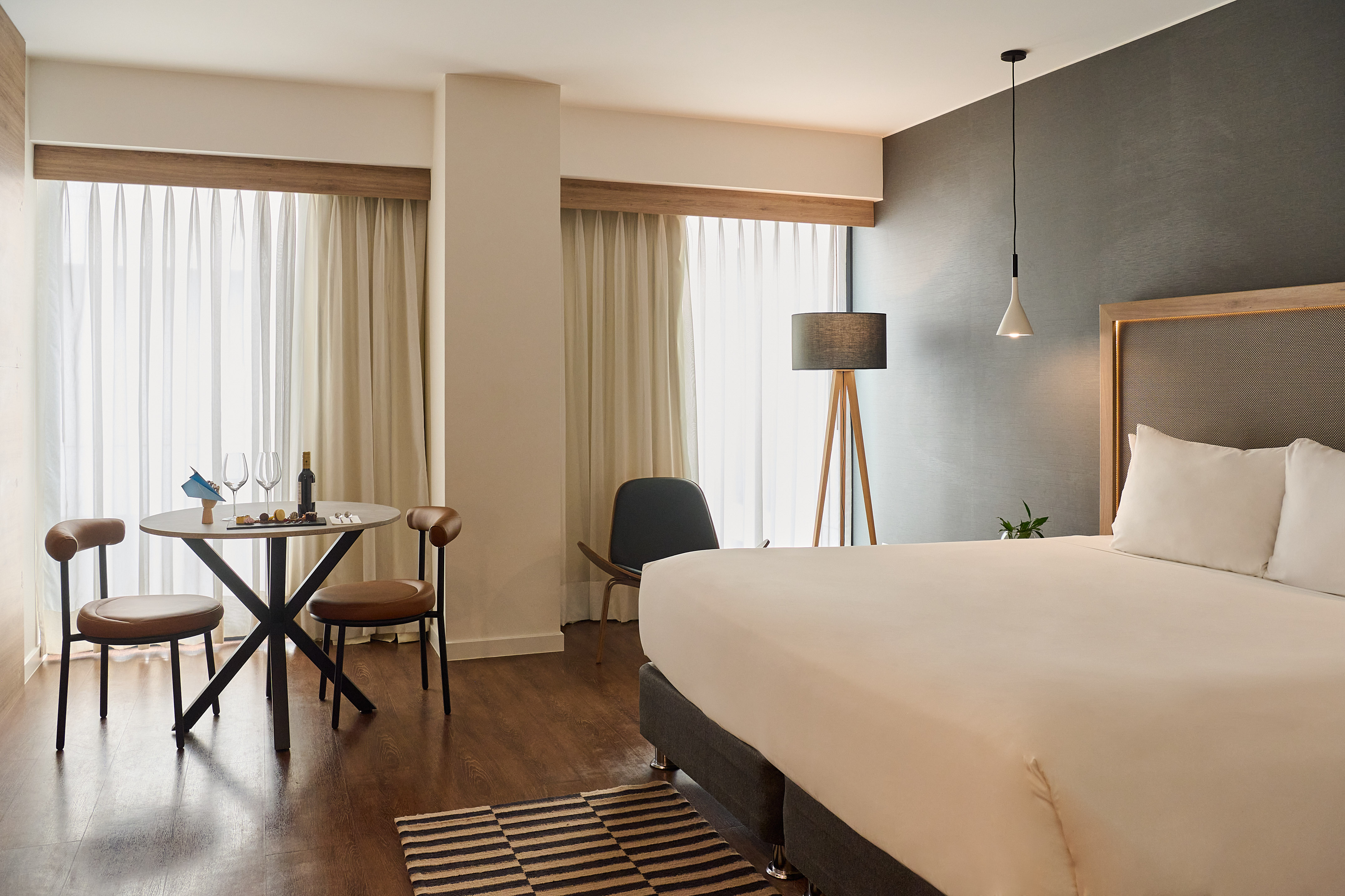 Modern hotel room with large bed, dining area, wine, and stylish decor.