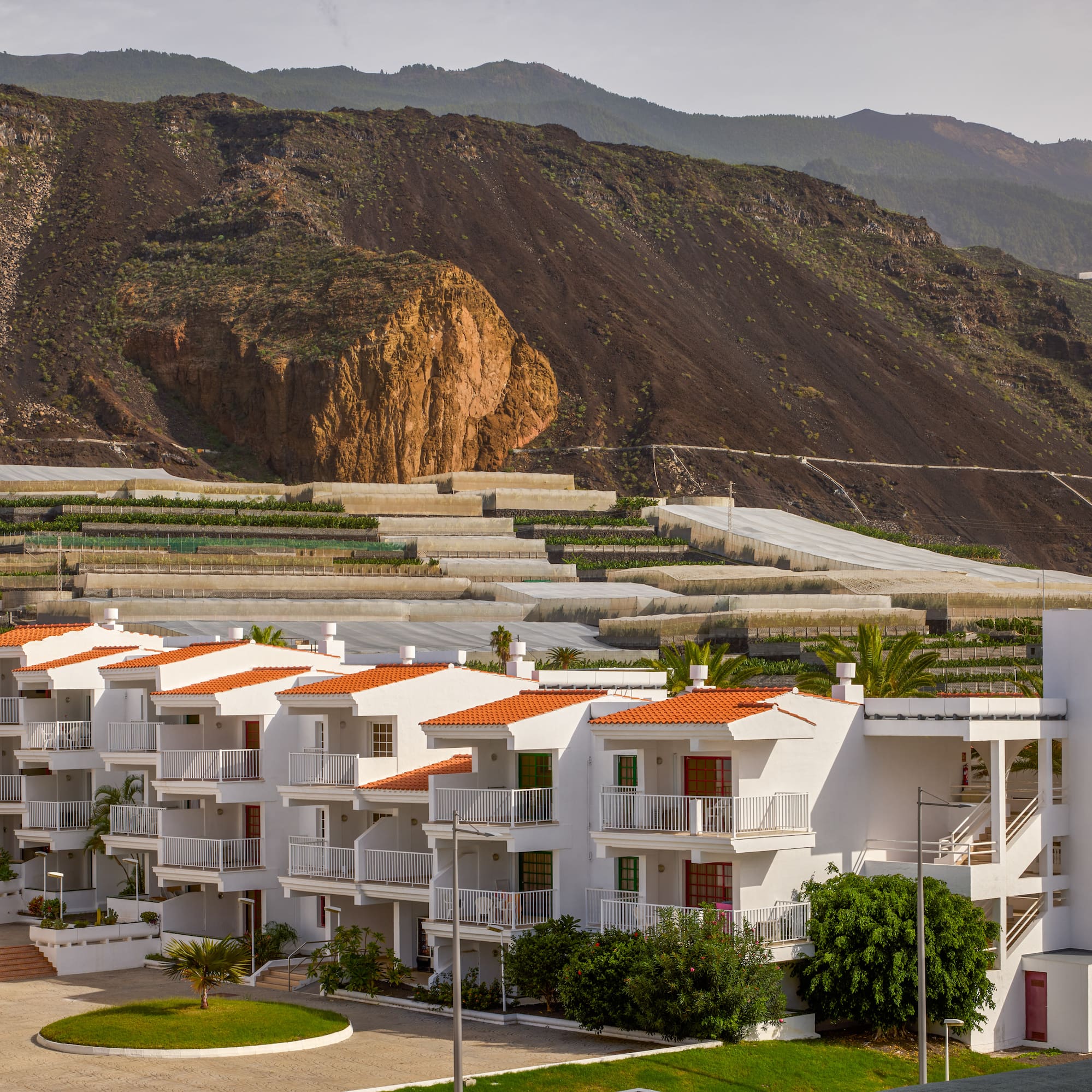a white building with orange roofs and a hill in the background