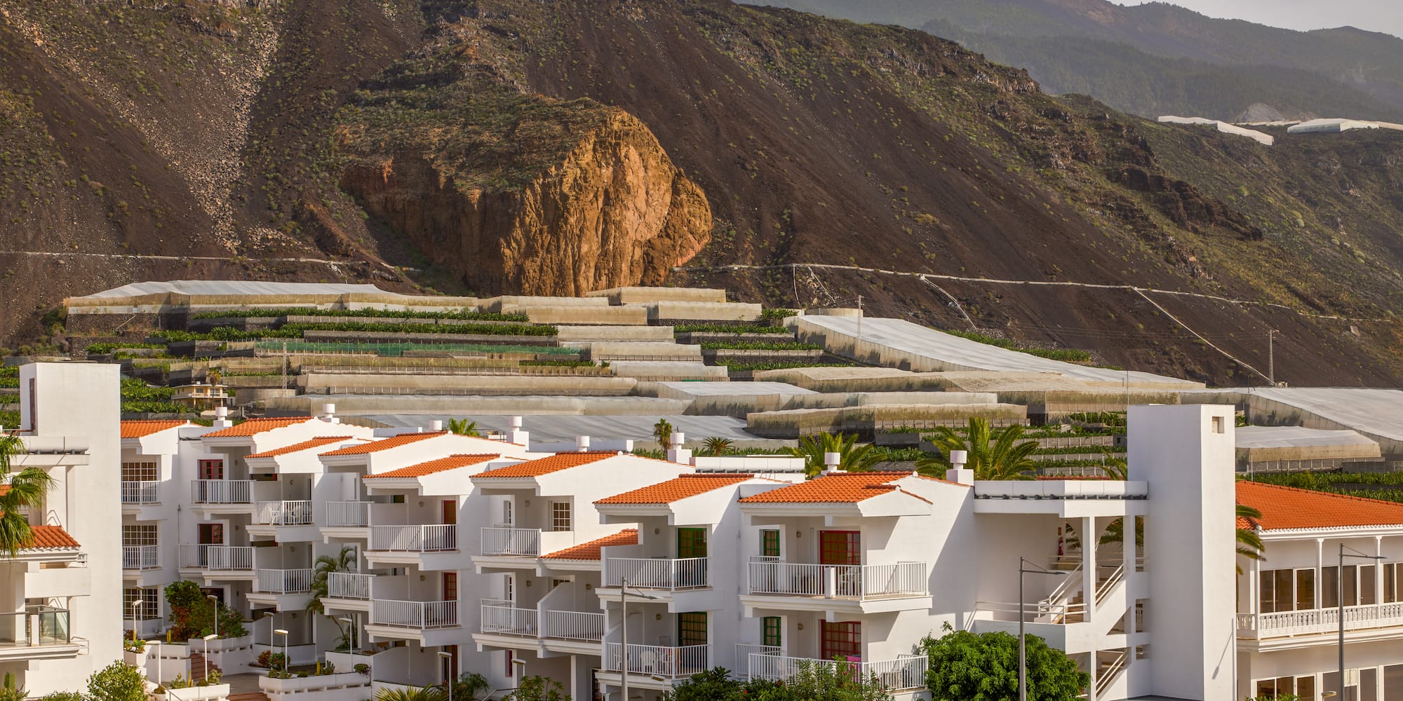 a white building with orange roofs and a hill in the background