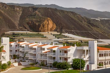 a white building with orange roofs and a hill in the background
