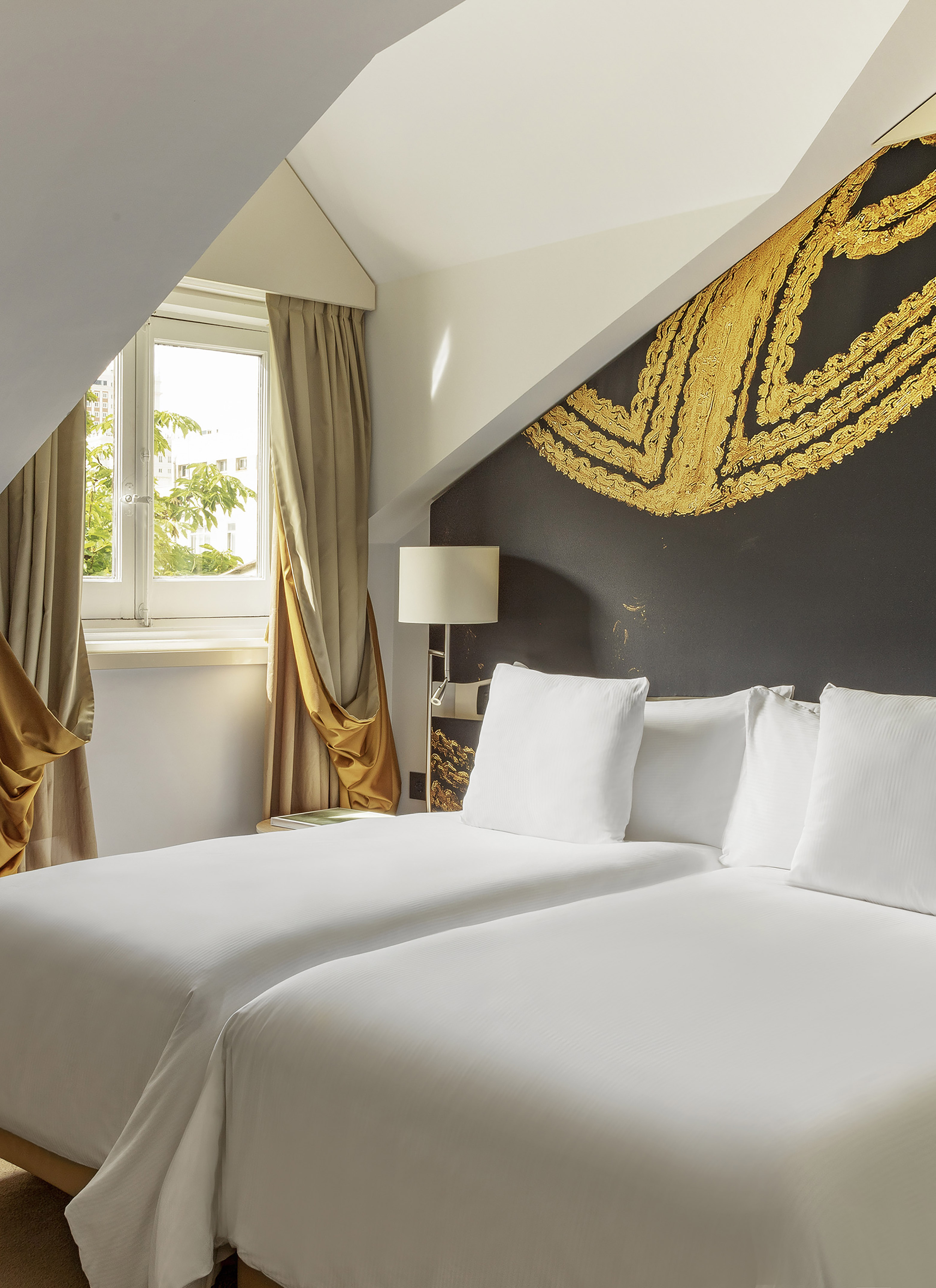Attic hotel room with two twin beds, natural light, and ornate gold wall art.