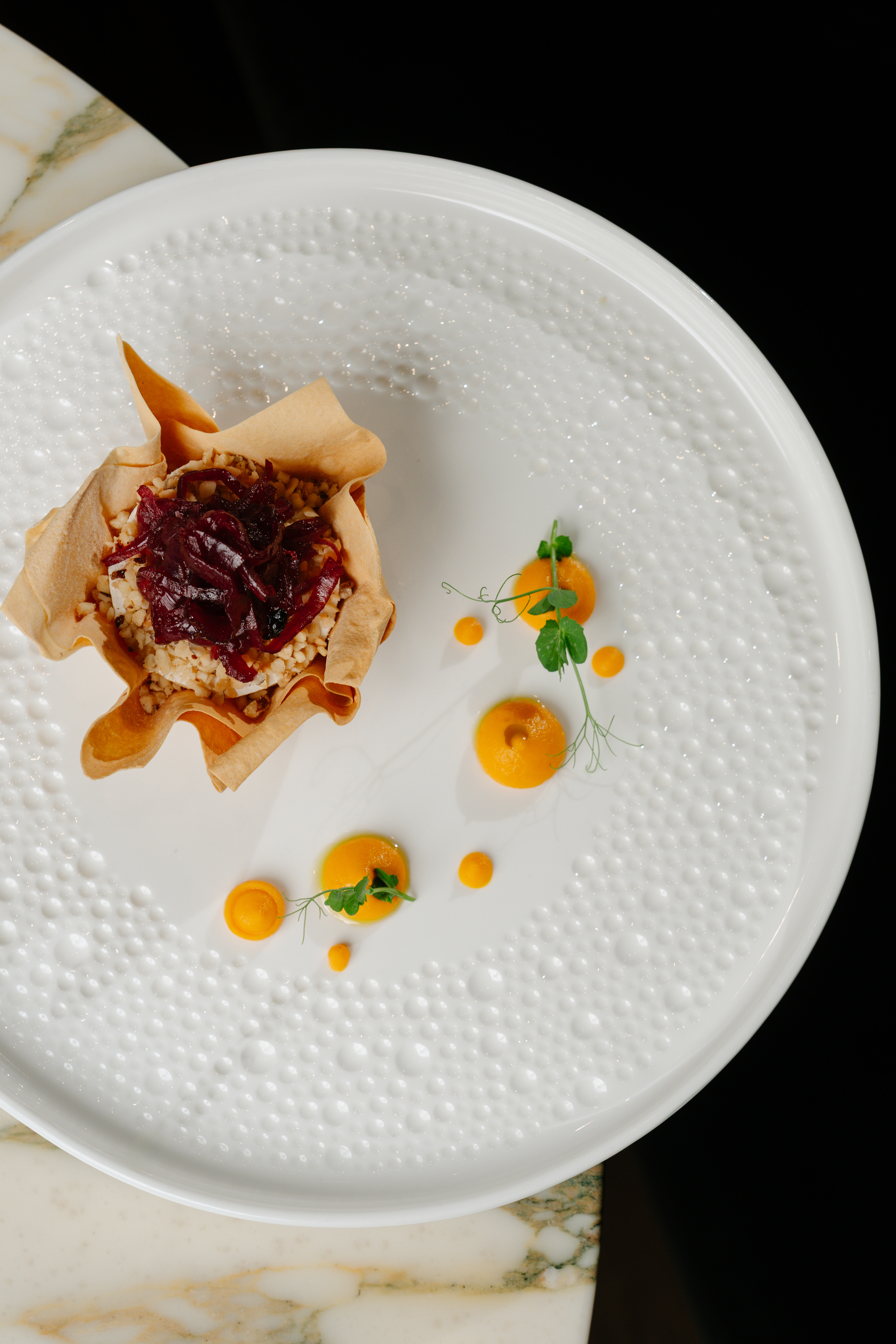 Gourmet tartlet with caramelized onions, orange puree, pea shoots on white plate.