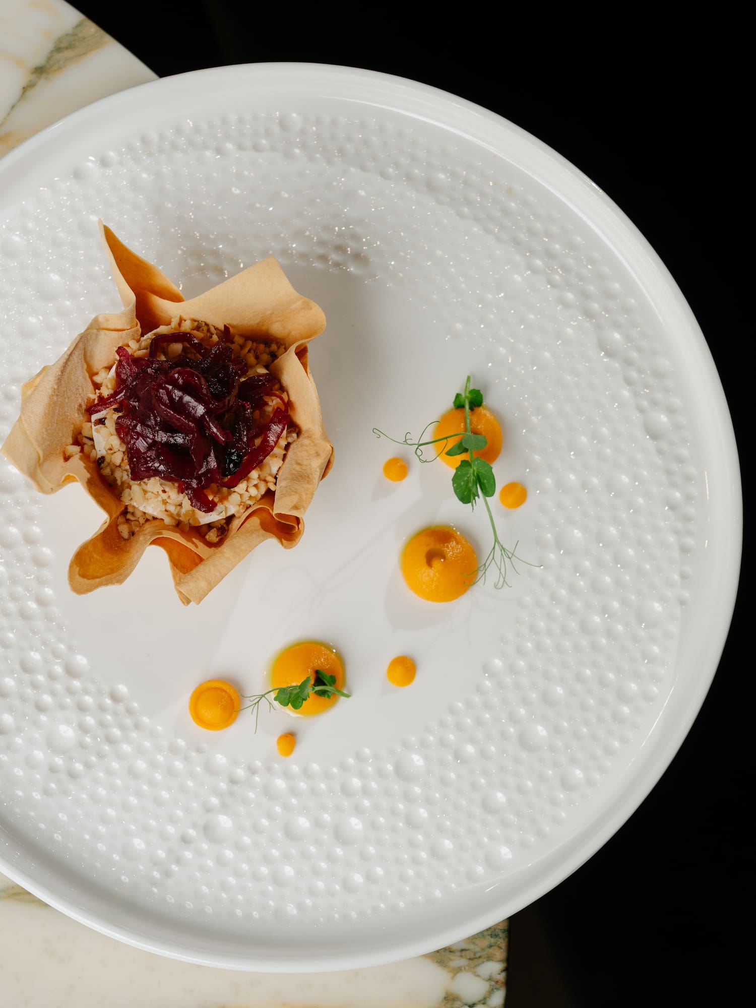 Gourmet tartlet with caramelized onions, orange puree, pea shoots on white plate.