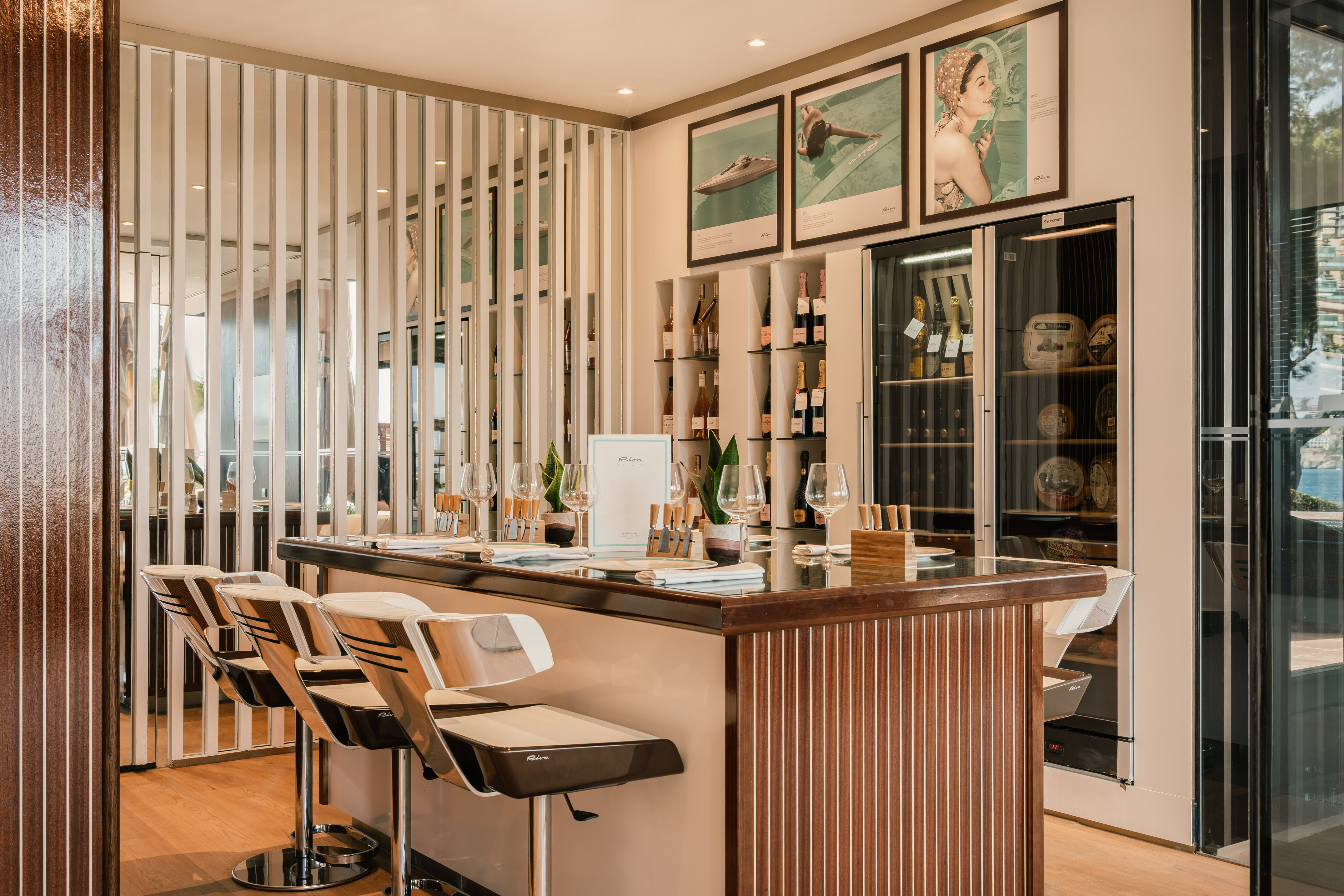 Luxury bar with Riva branding, wine cooler, sleek stools, and sea view.