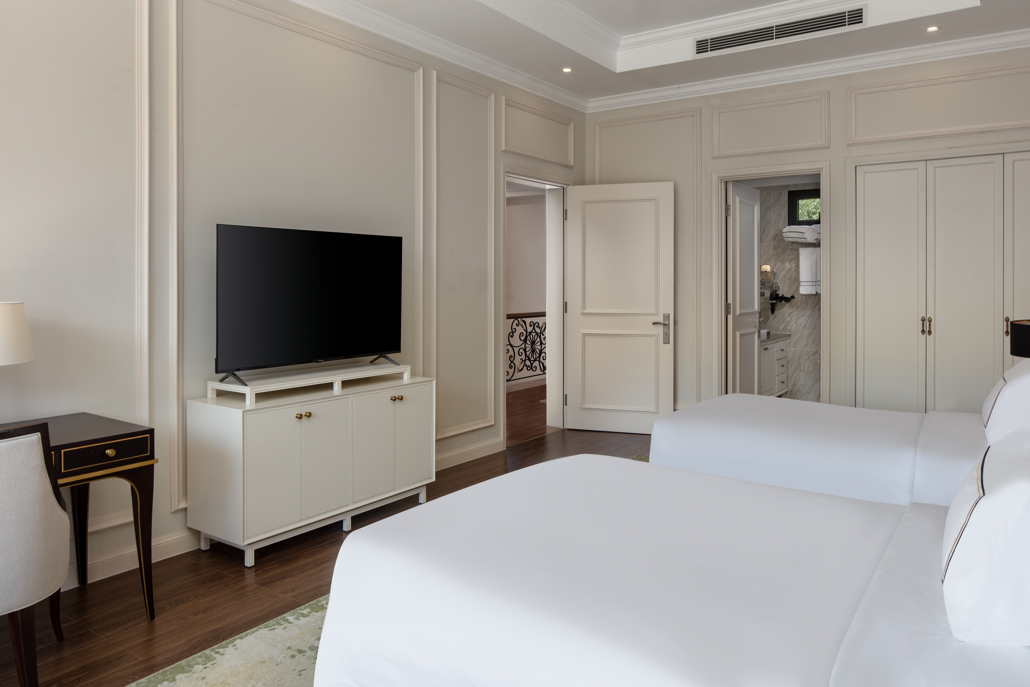 Twin hotel room with TV, white beds, paneled walls, and hardwood floor.