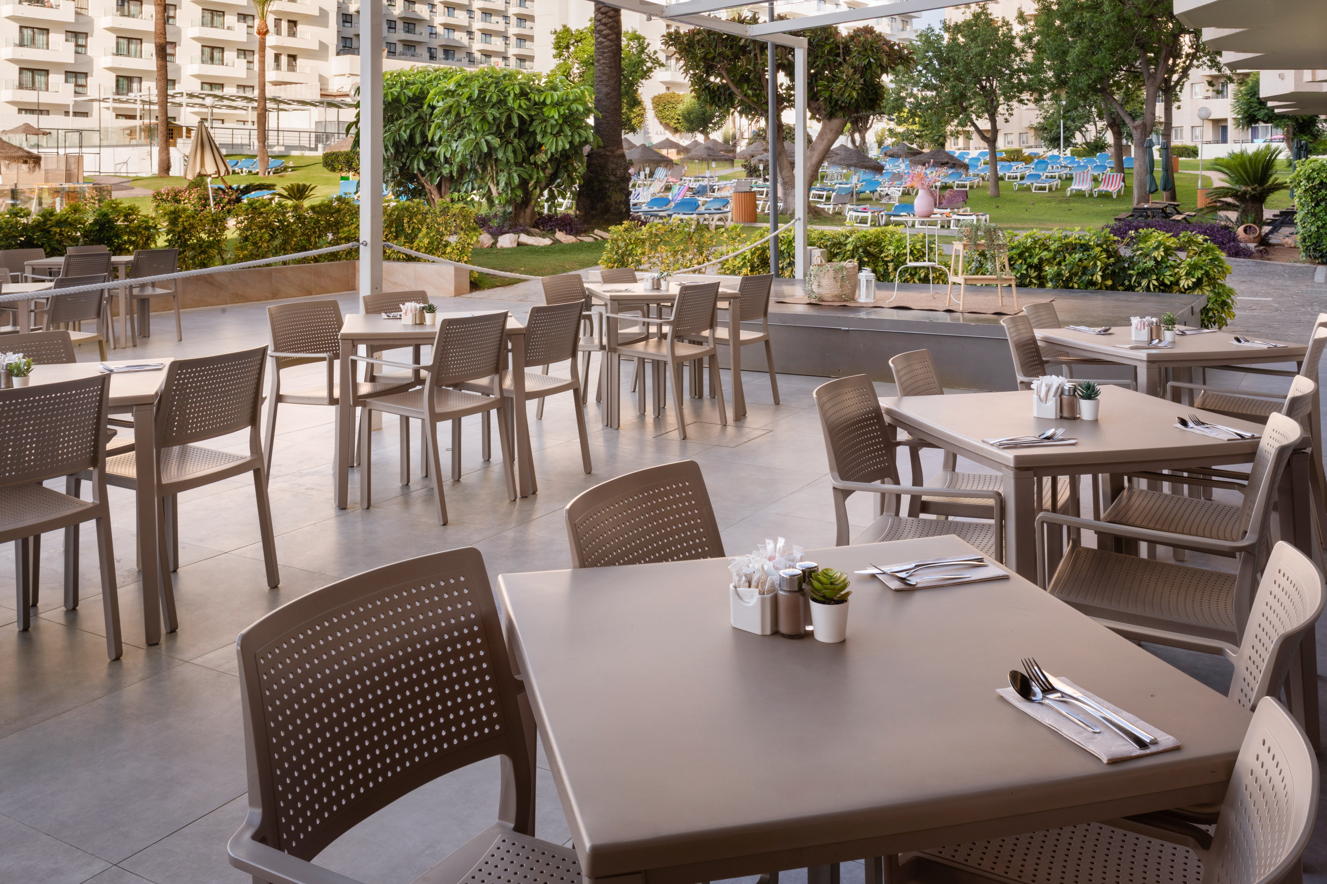 Set tables on an outdoor dining terrace at a lush resort hotel.