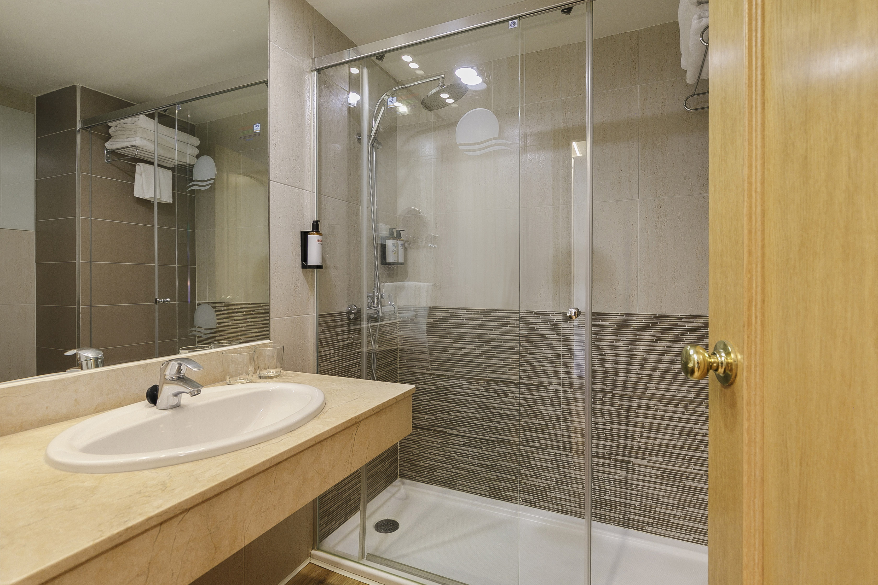 Modern bathroom with walk-in glass shower, vanity sink, and mosaic wall tiles.