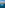 Sailboat in clear turquoise bay with beach, coastal homes, and pines.