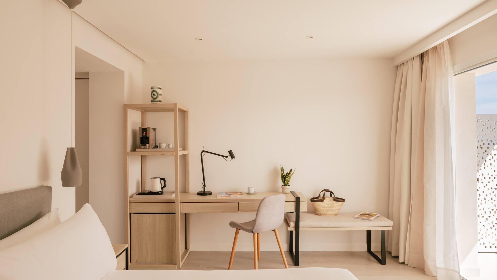 Bright, modern hotel room with minimalist desk, coffee station, and bed.