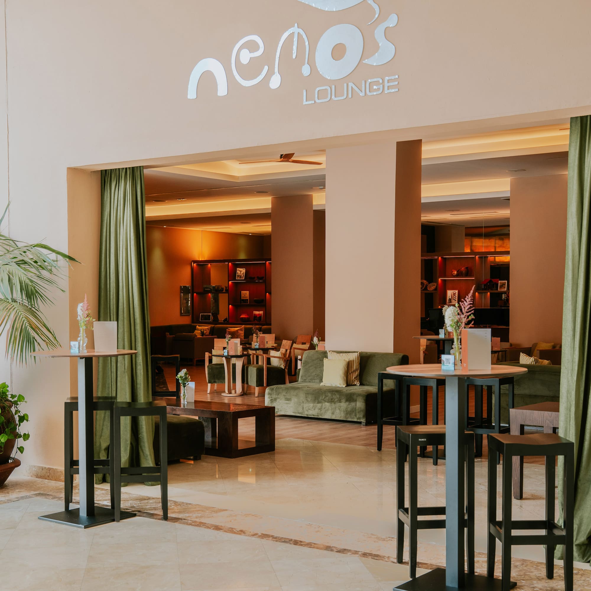 Nemo's Lounge entrance with high tables, green sofas, and warm lighting.