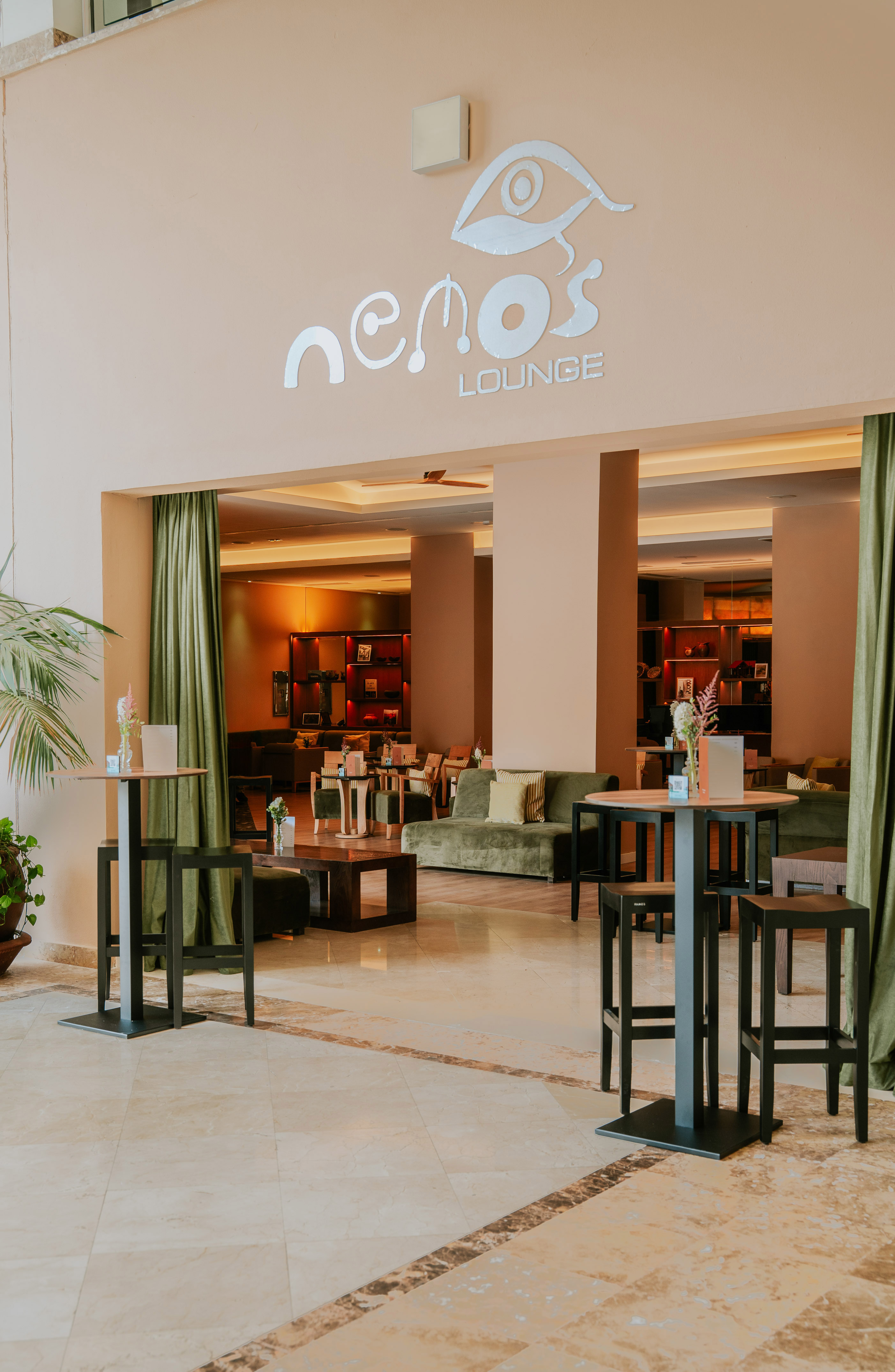 Nemo's Lounge entrance with high tables, green sofas, and warm lighting.