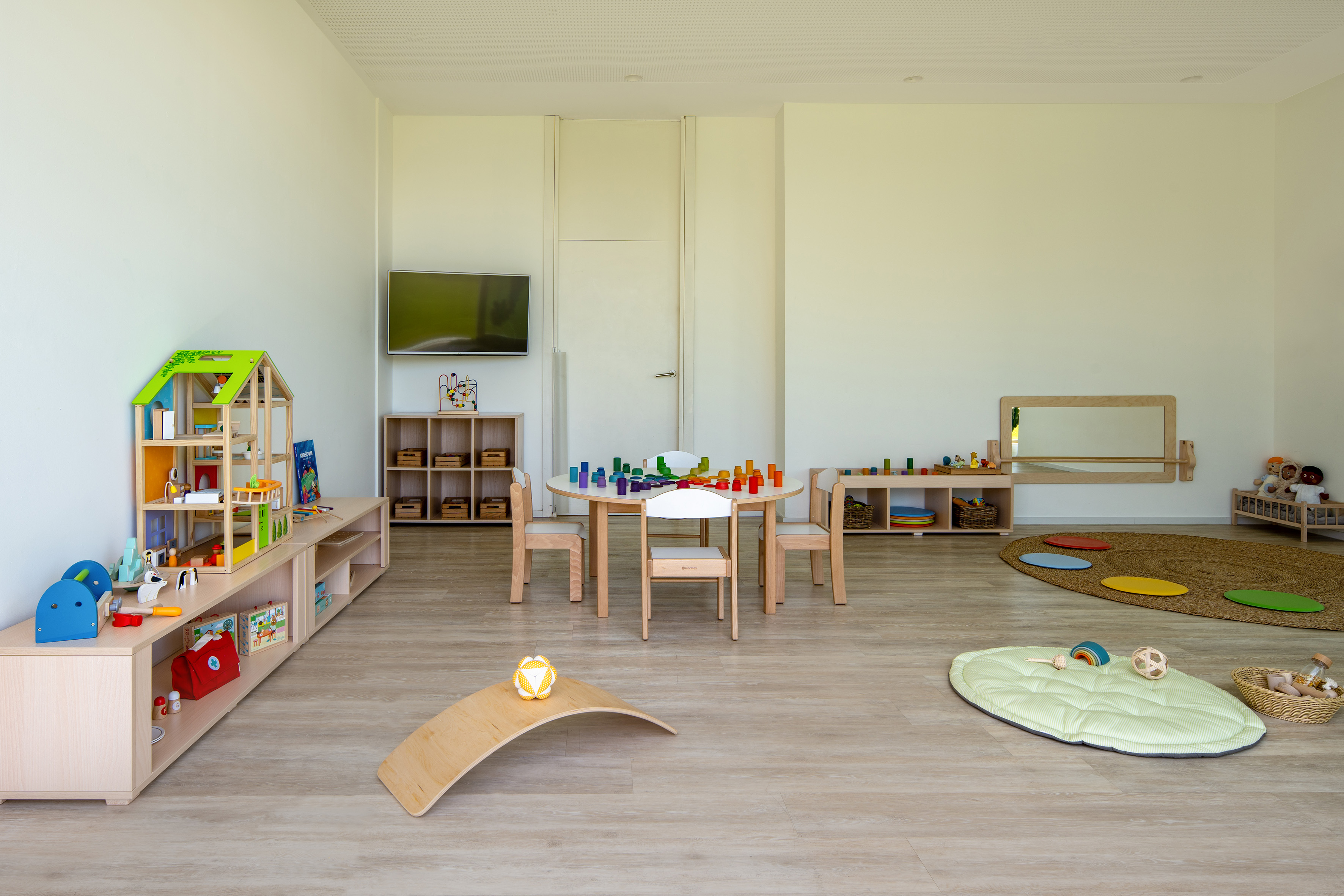 Bright children's playroom with wooden toys, activity table, chairs, and play mats.