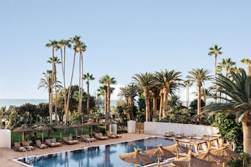 a pool with lounge chairs and umbrellas and palm trees