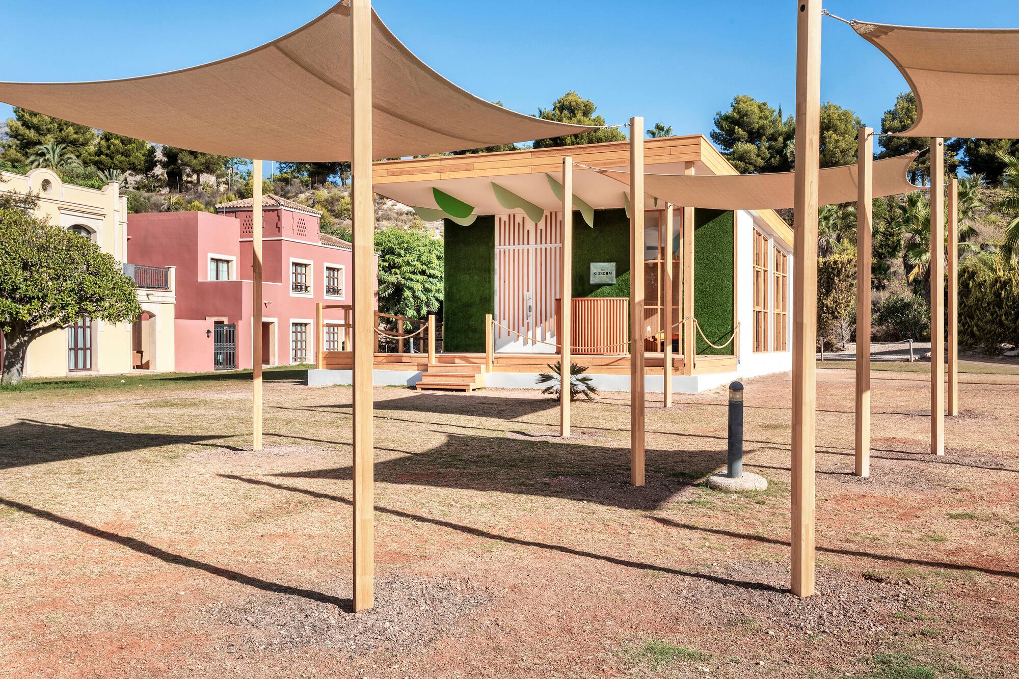 Outdoor Kidsom children's club, green wall facade, wood deck, and shade sails.