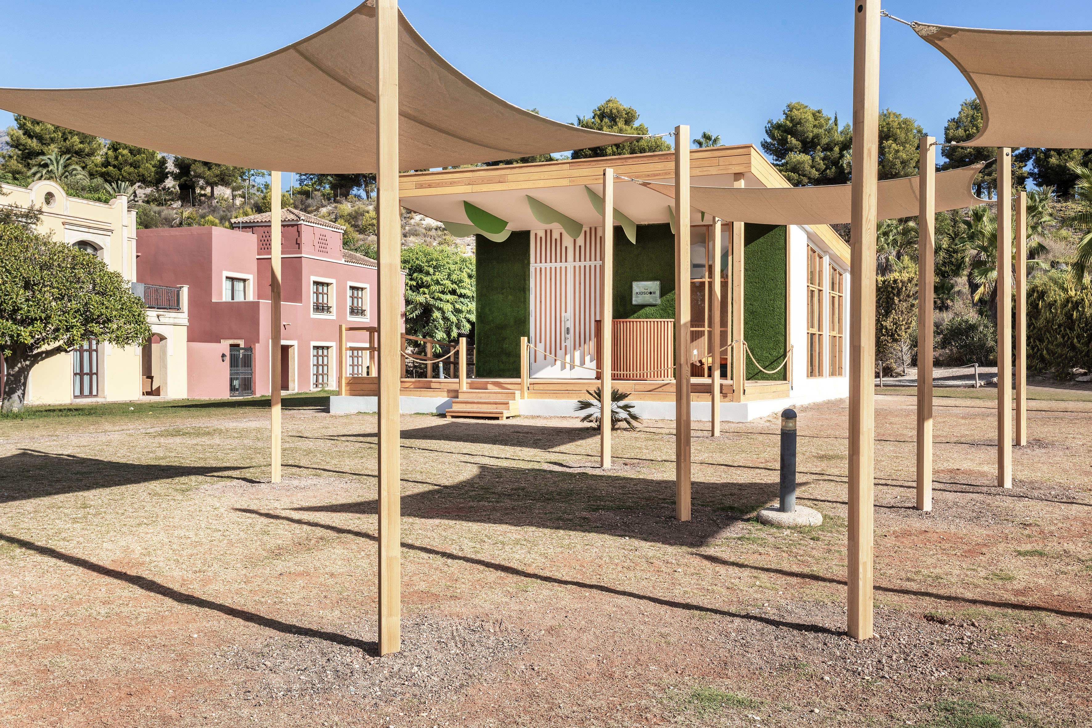 Outdoor Kidsom children's club, green wall facade, wood deck, and shade sails.
