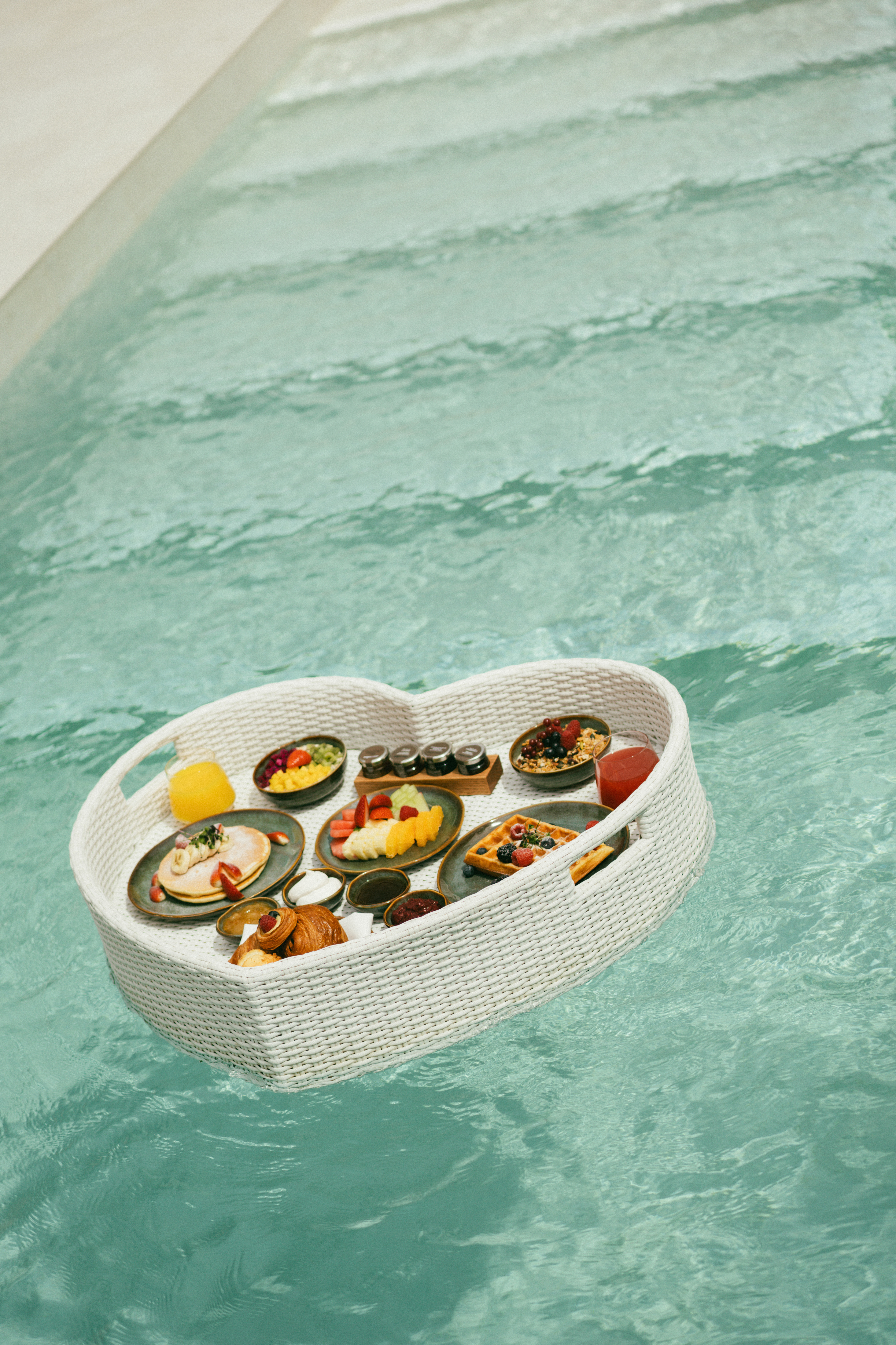 Floating heart-shaped breakfast tray with waffles, fruit, pancakes in pool.