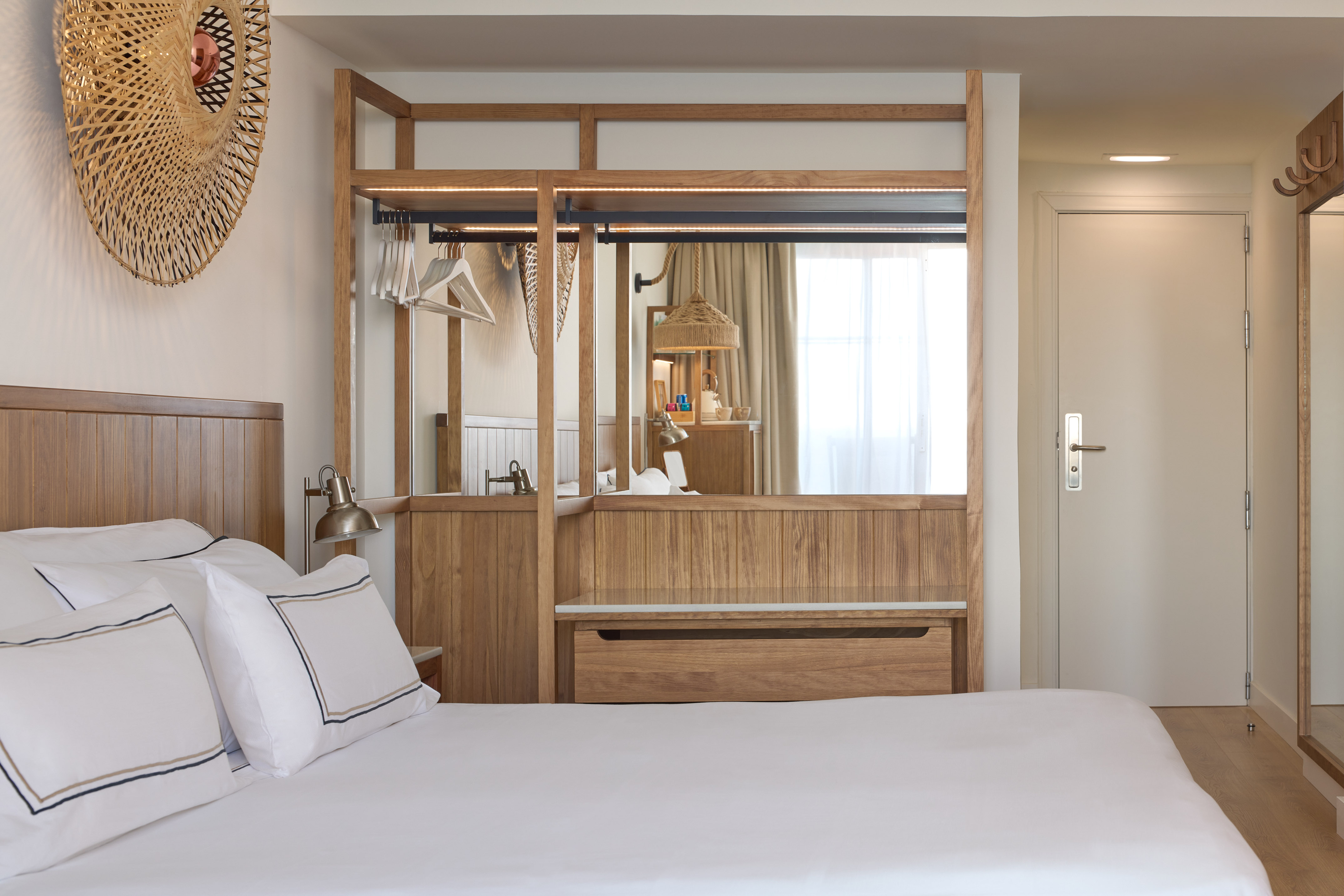 Modern hotel bedroom with king bed, wood accents, mirror, and woven decor.