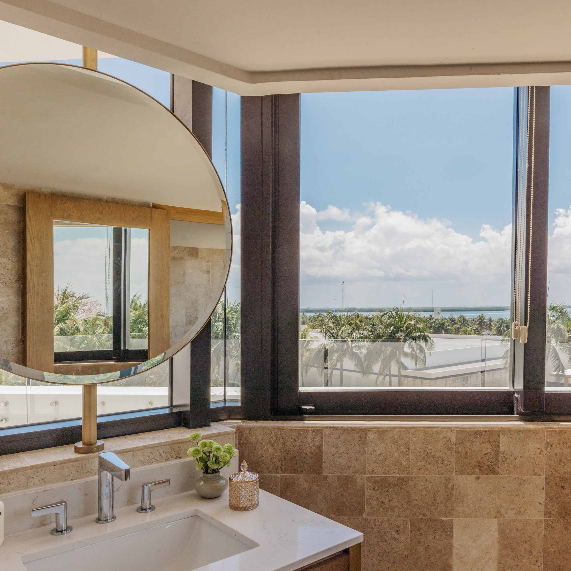 Modern bathroom vanity, round mirror, and large window with tropical ocean view.