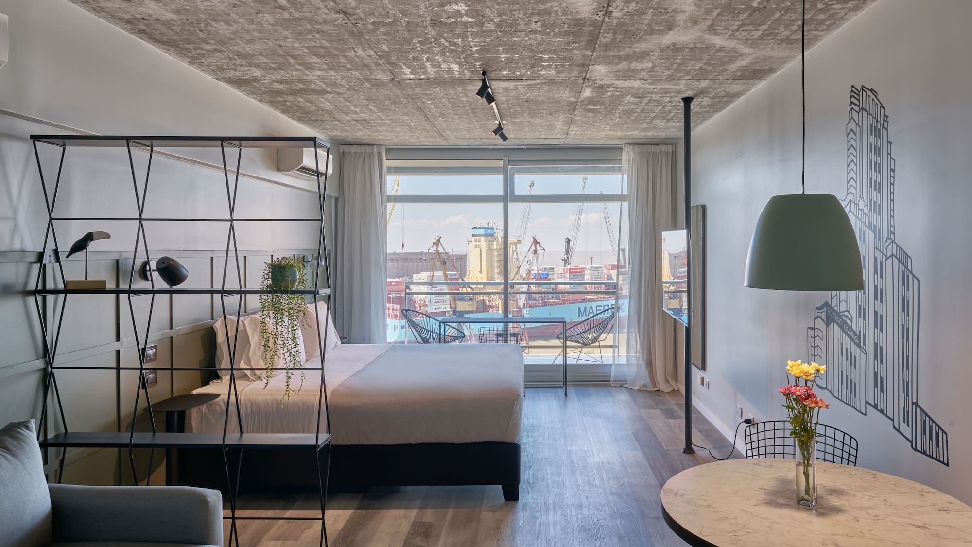 Modern industrial studio with port view, concrete ceiling, and bedroom.