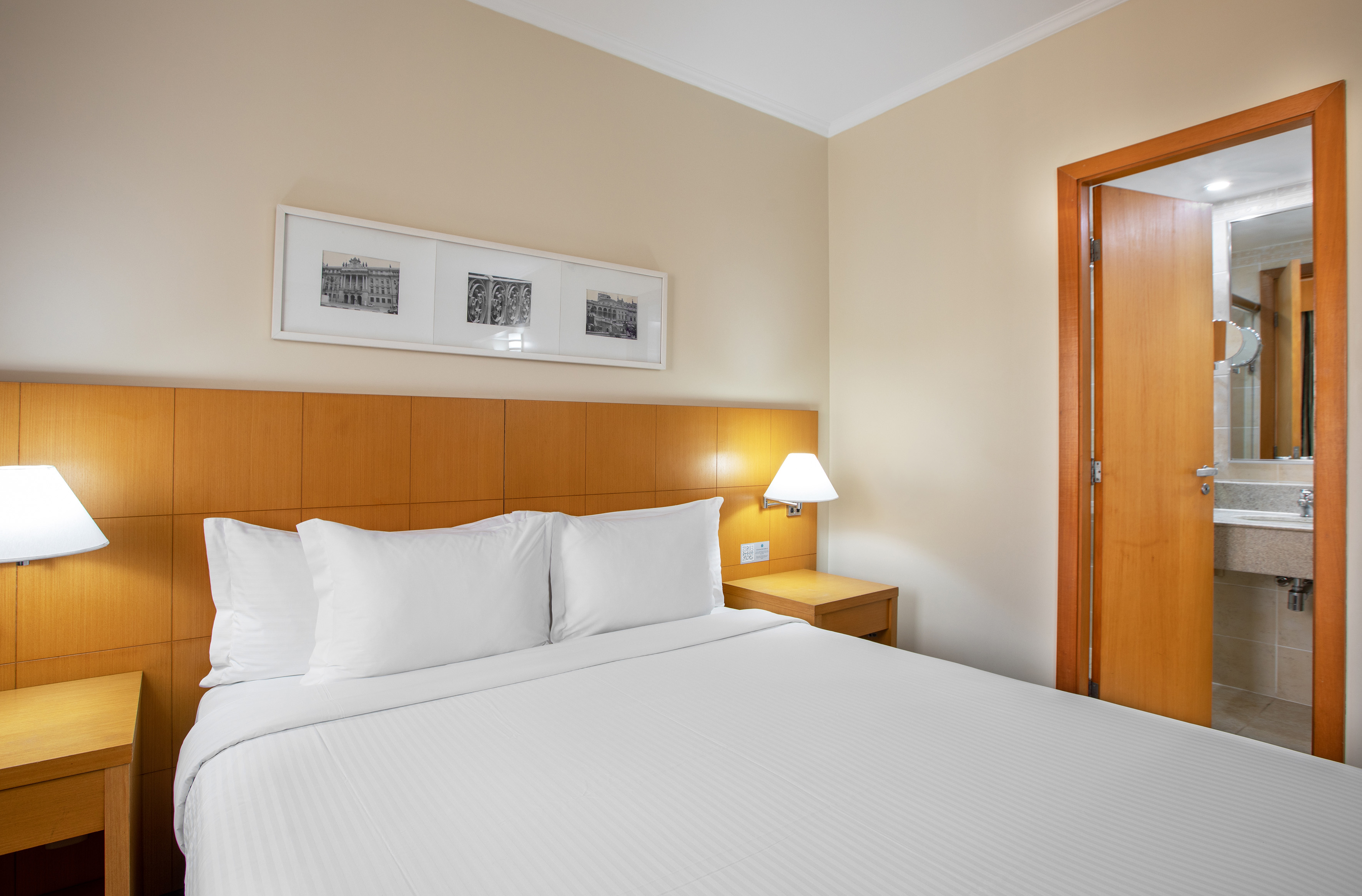 Hotel room with clean white bed, wooden headboard, bedside lamps, and bathroom.