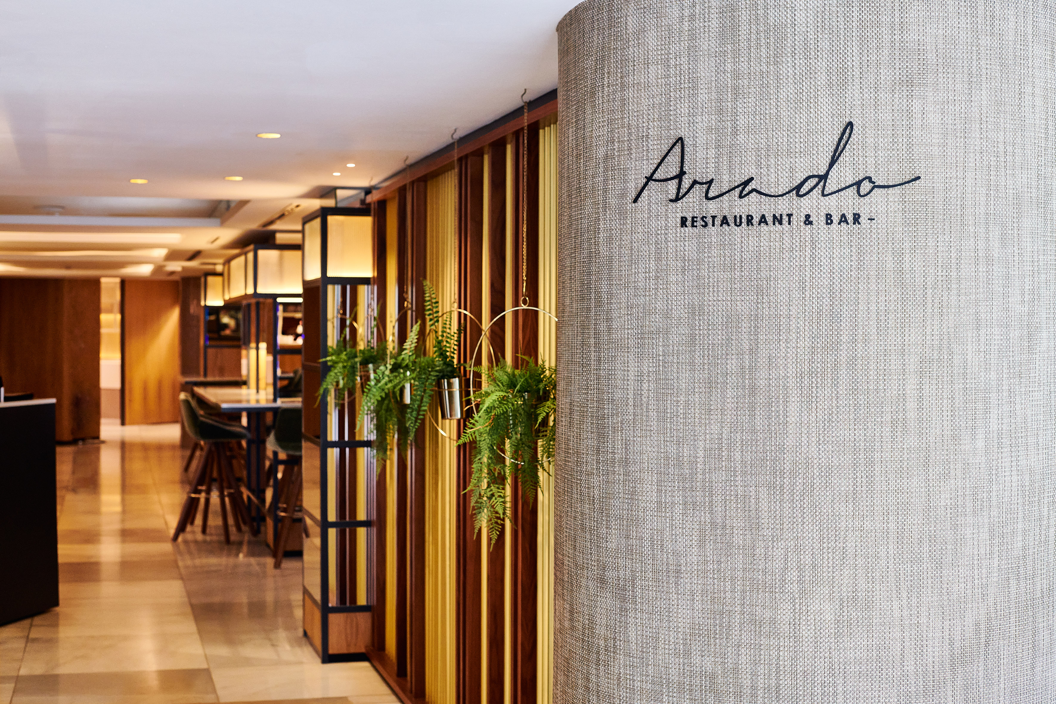 Arado Restaurant & Bar sign on textured column, modern interior, hanging plants.