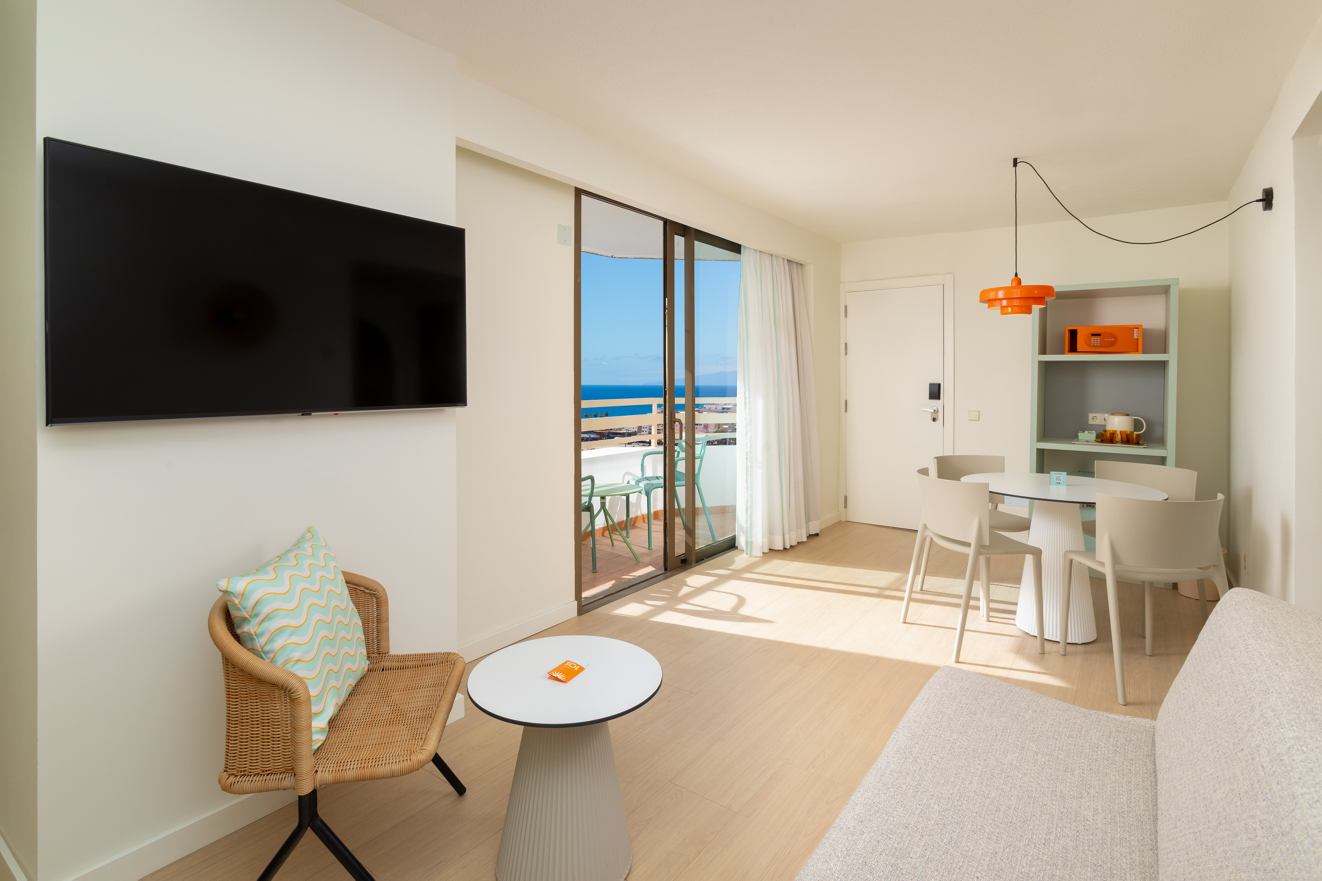 Bright hotel apartment with sea view balcony, TV, and dining area.