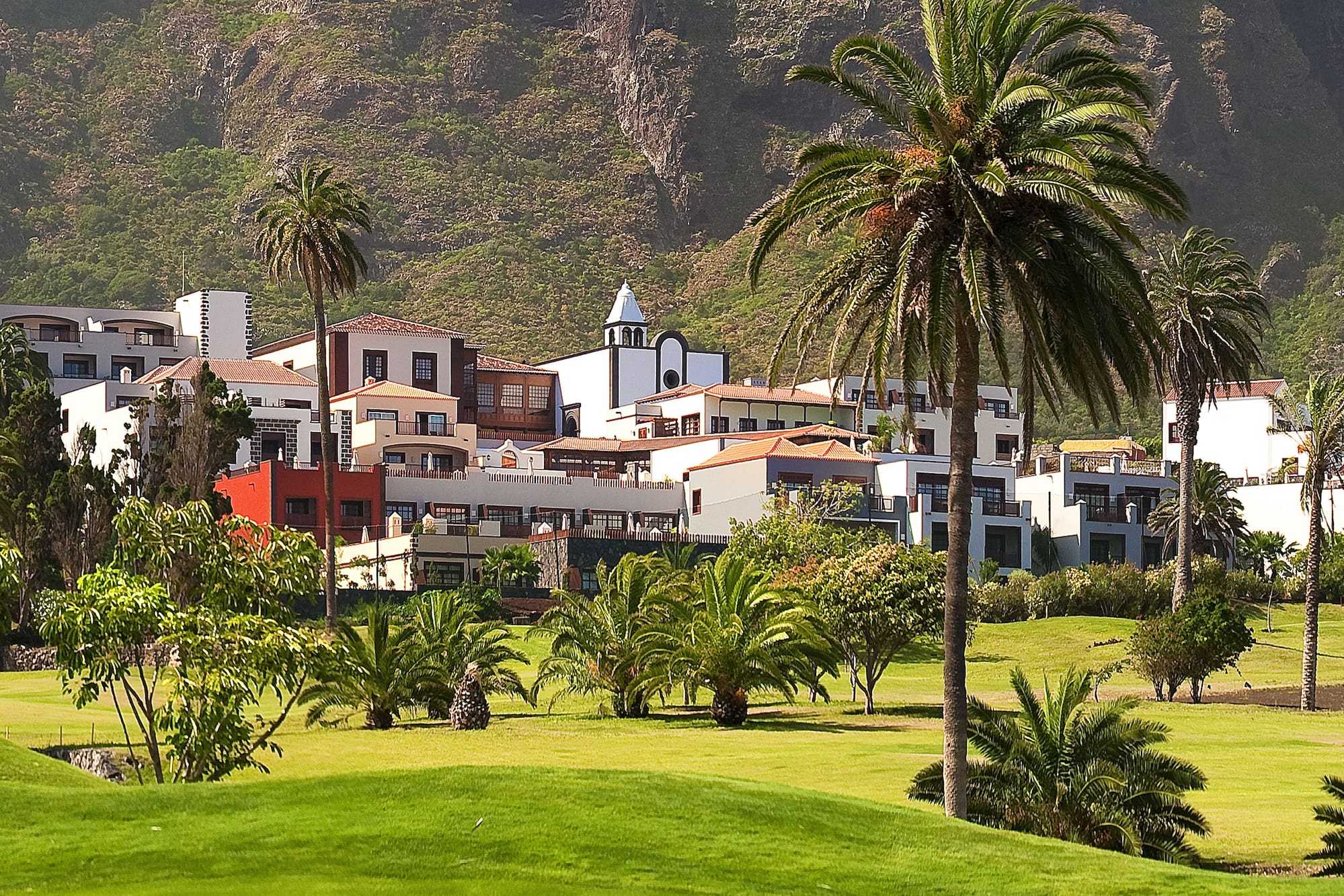 Mountain resort with palm trees, white buildings, and a lush green golf course.