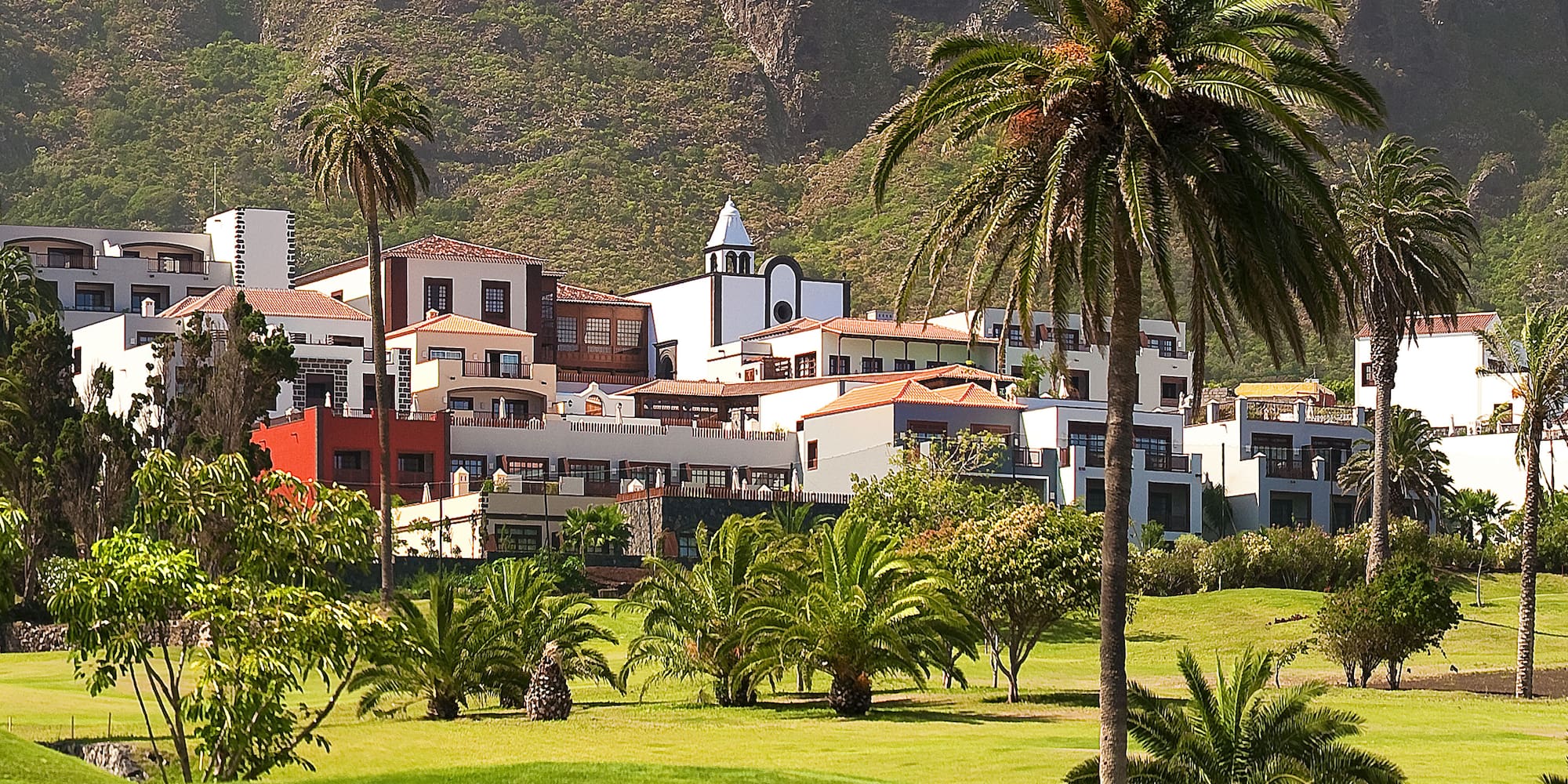 Mountain resort with palm trees, white buildings, and a lush green golf course.