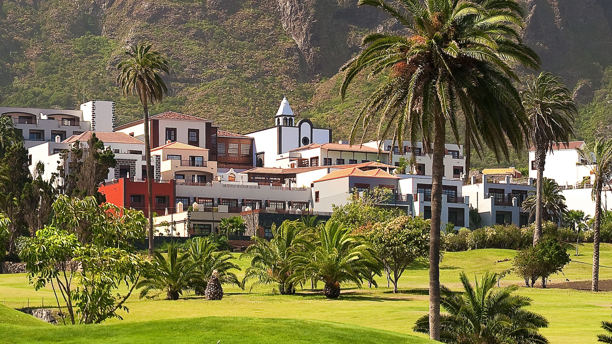 Mountain resort with palm trees, white buildings, and a lush green golf course.